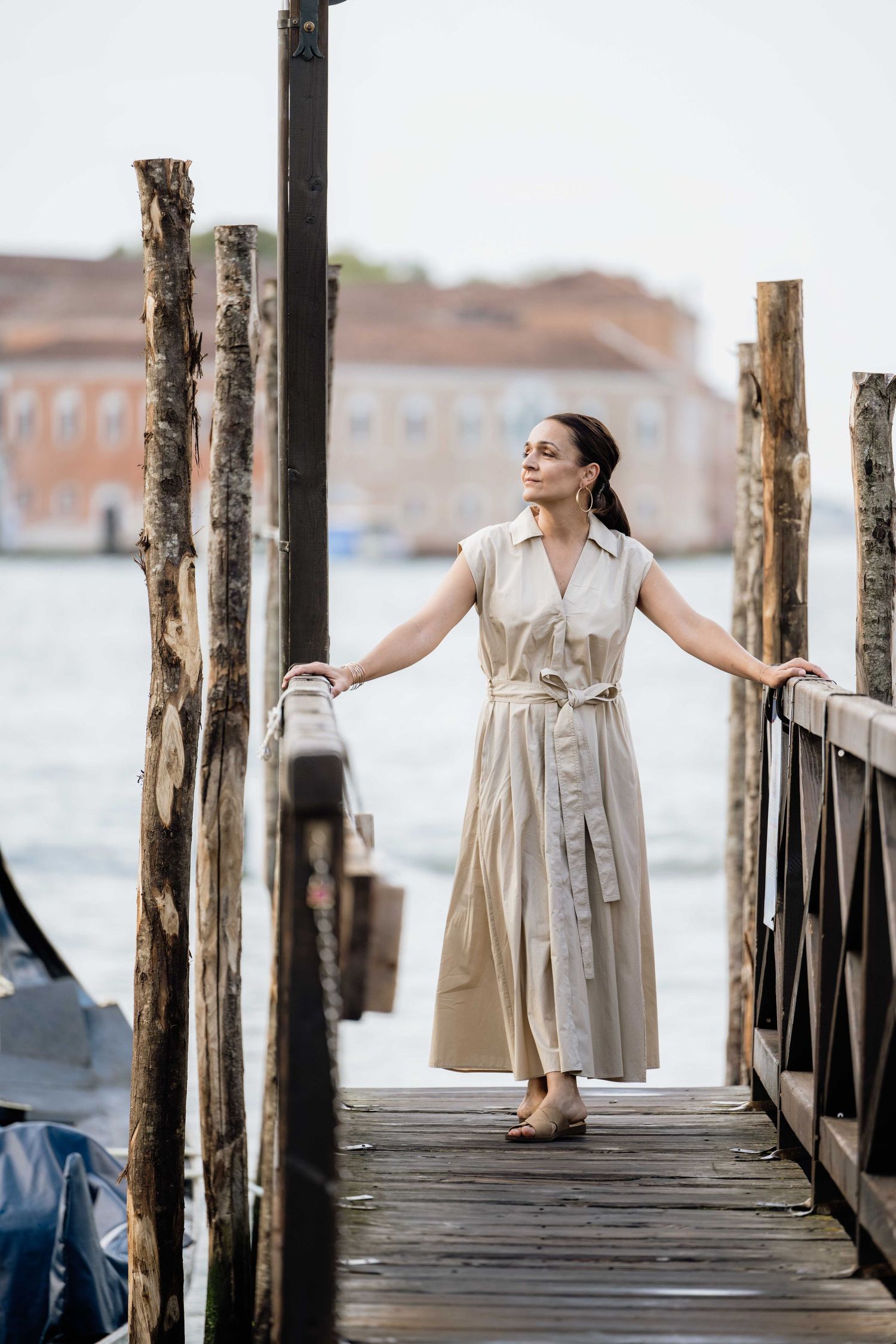 Person in light dress posing on wooden dock with gondolas and Venice lagoon in background.
