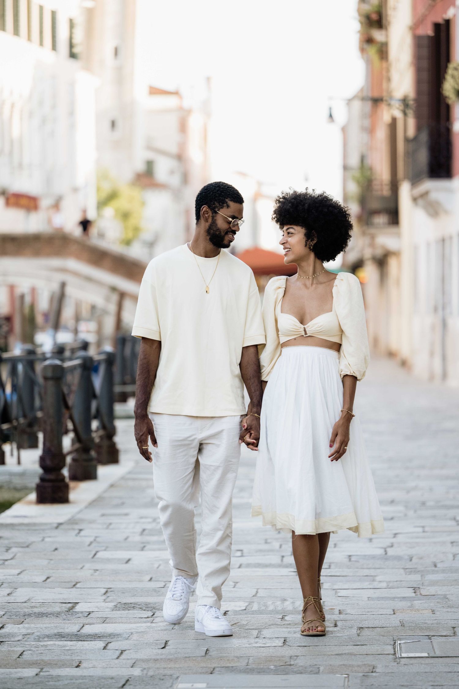 A couple walking together on a European street wearing coordinated white summer outfits.