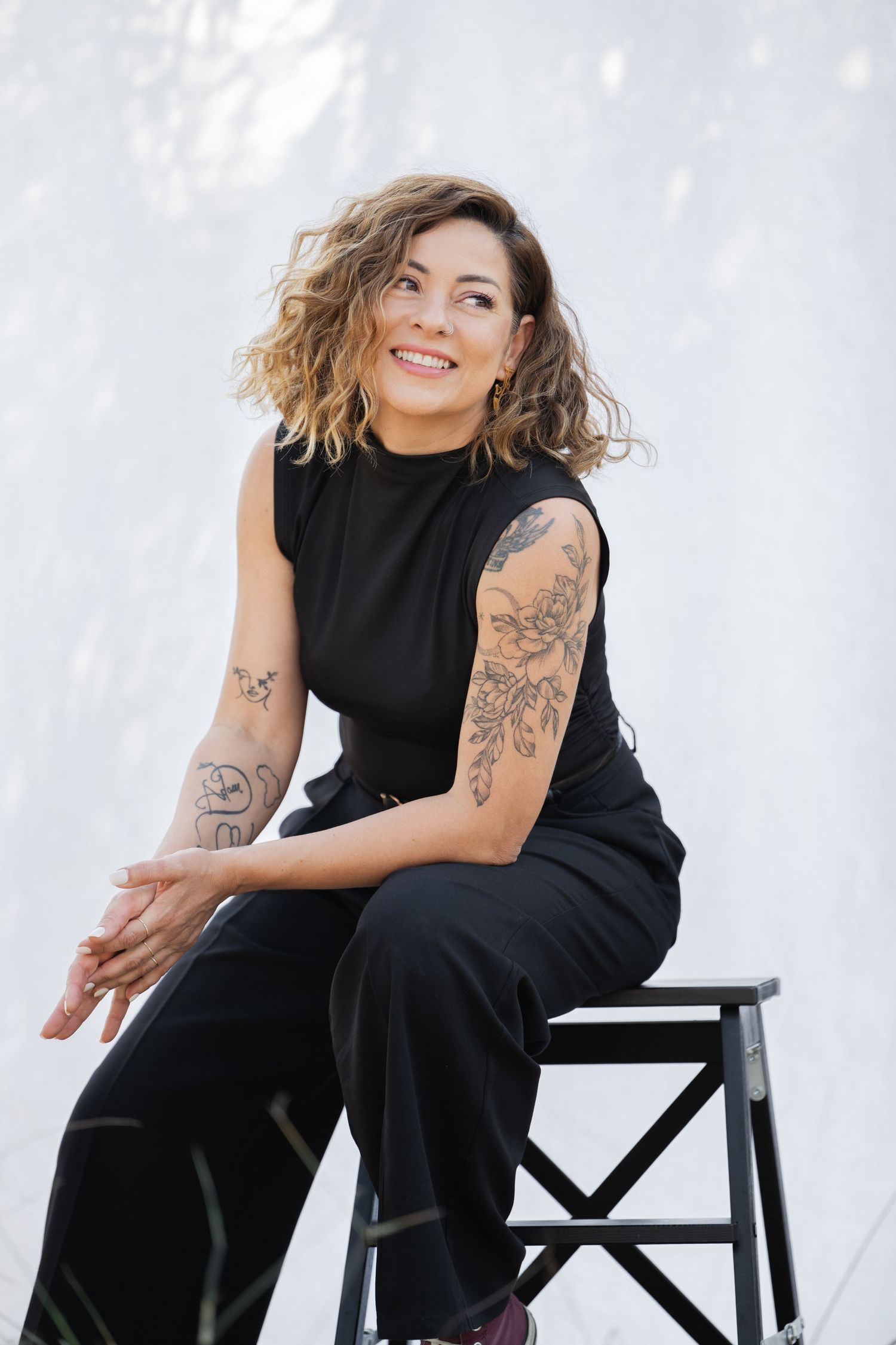 Professional portrait session featuring casual black outfit and tattoos against white backdrop.