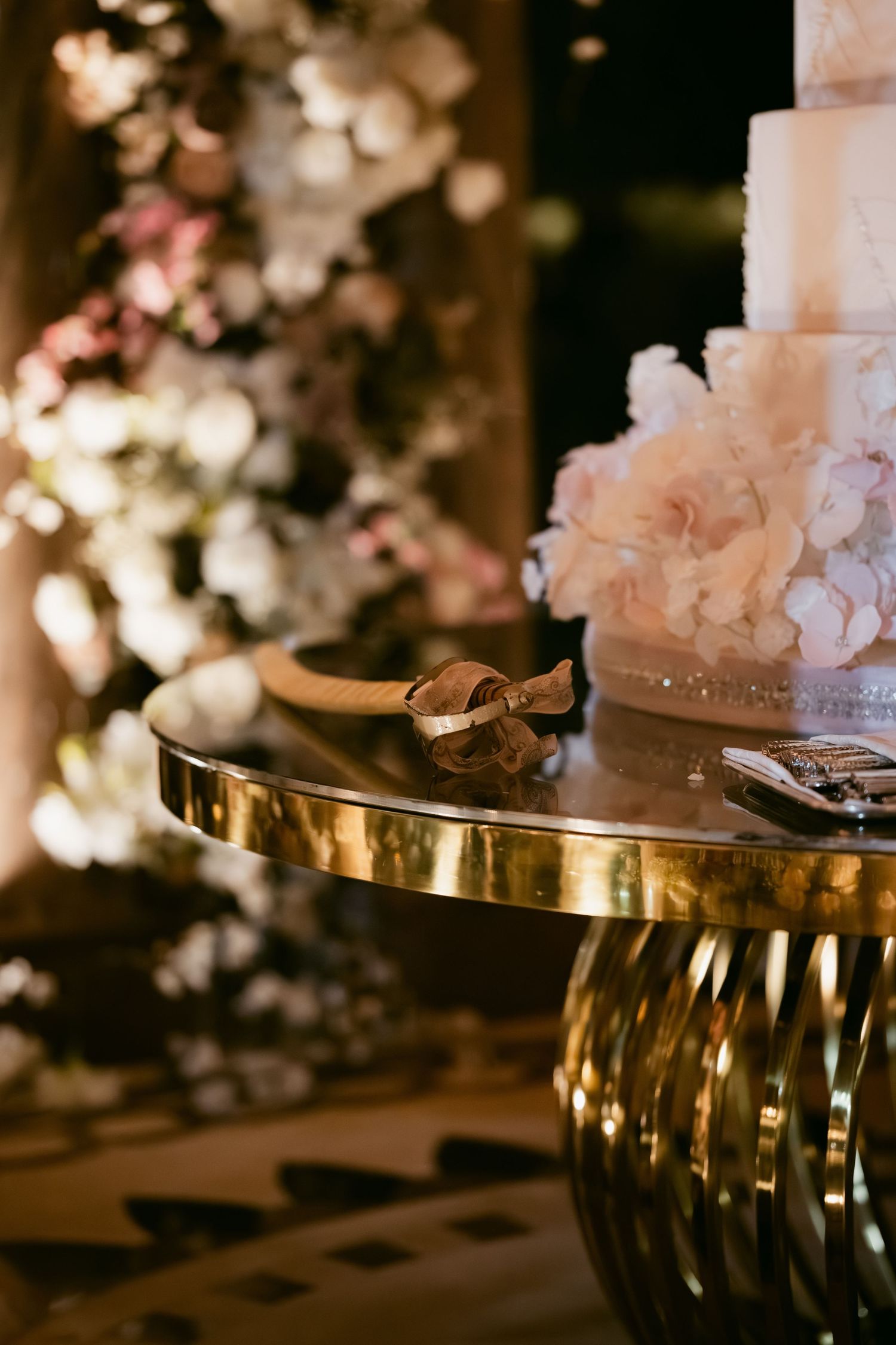 Elegant white wedding cake displayed on a gold mirrored stand with floral decorations.