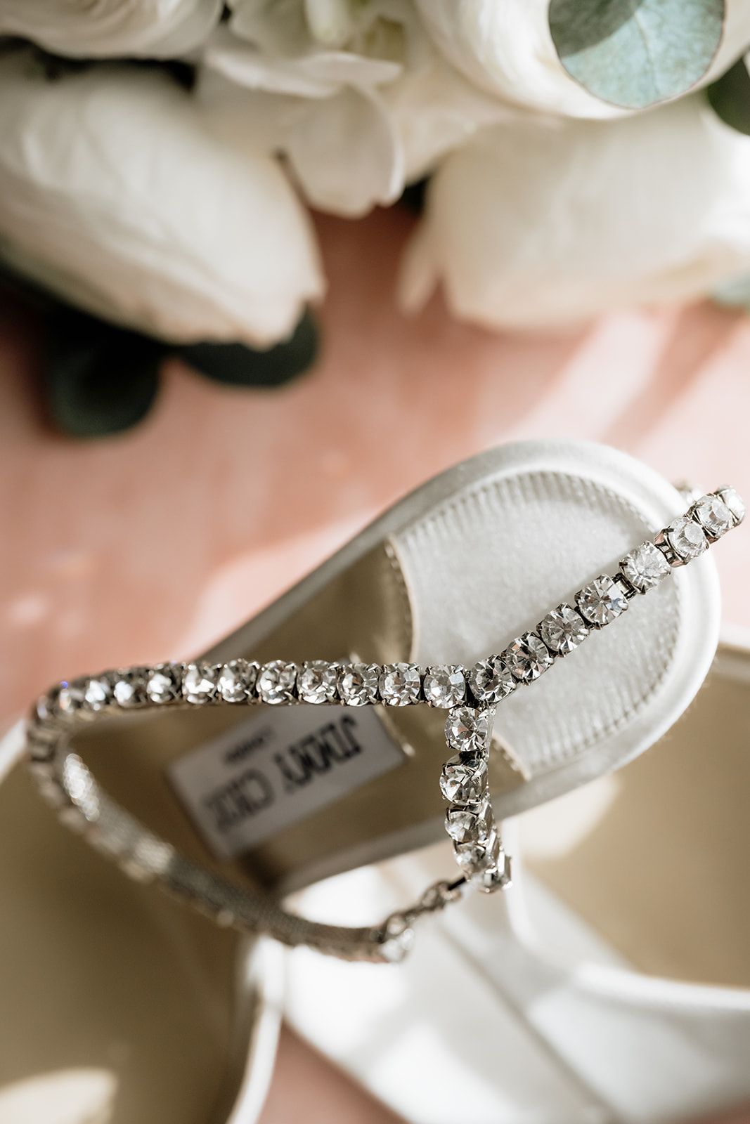Crystal-embellished bridal shoes with rhinestone straps against a soft blush background.