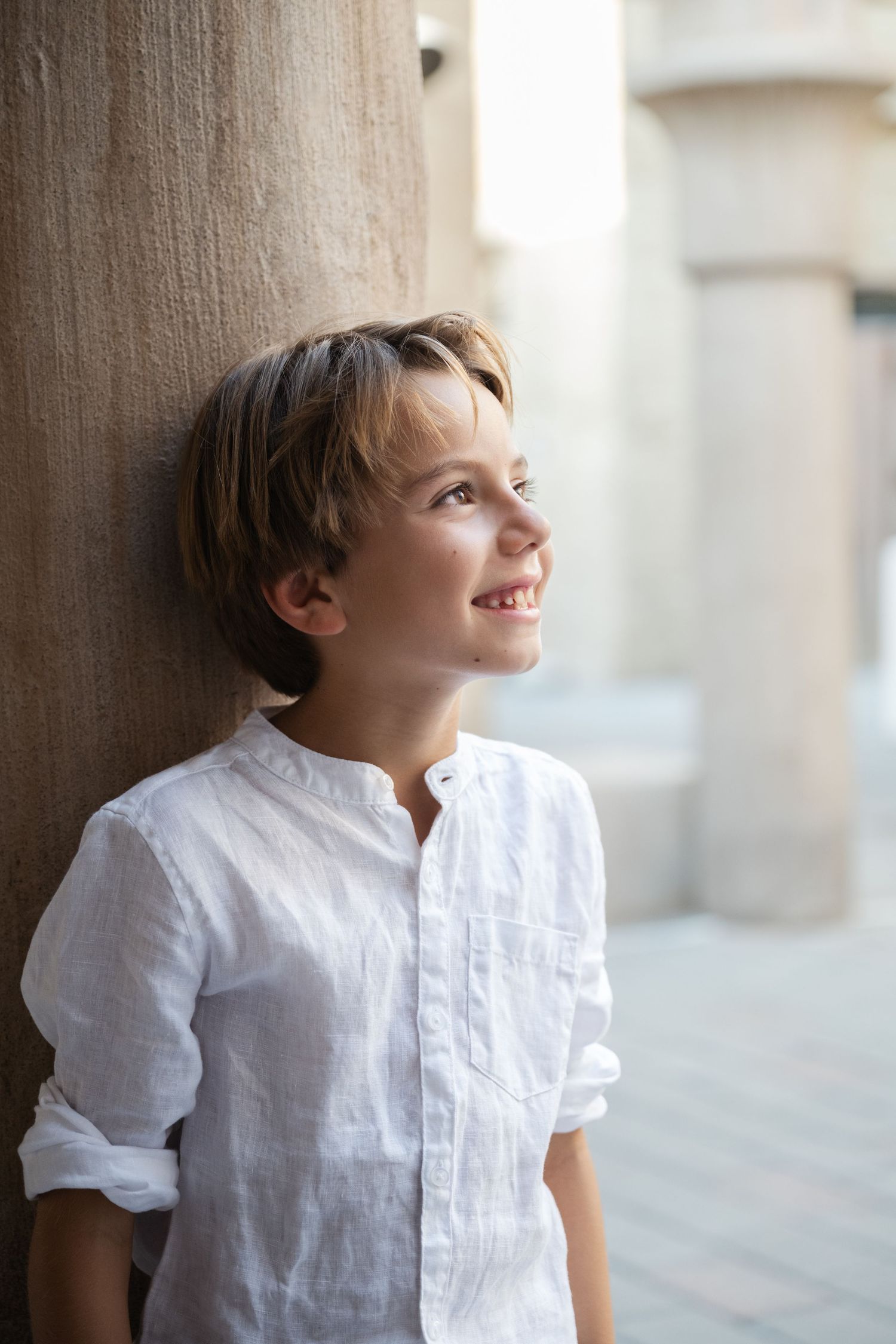 Child in white shirt smiling while standing against stone pillars.