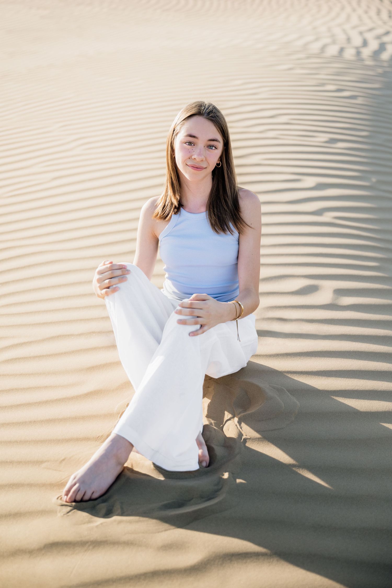 Person in white attire poses gracefully on rippled desert sand.