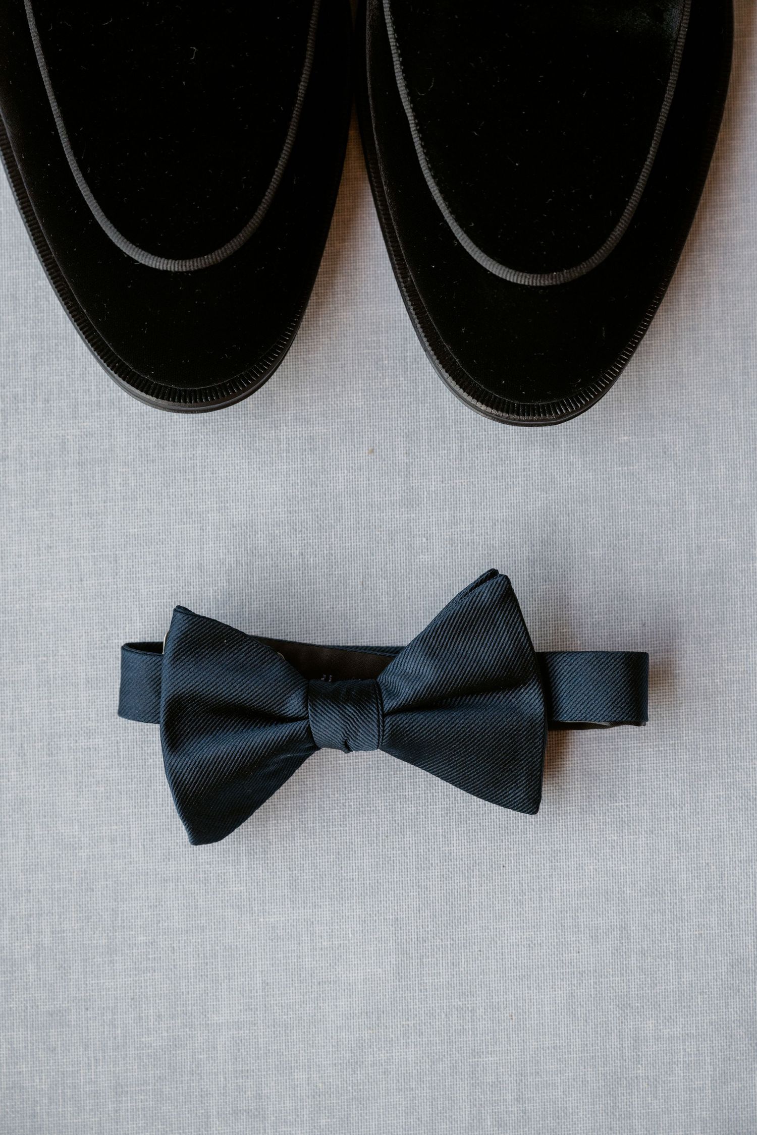 Three classic black bow ties arranged in a row on light gray fabric.