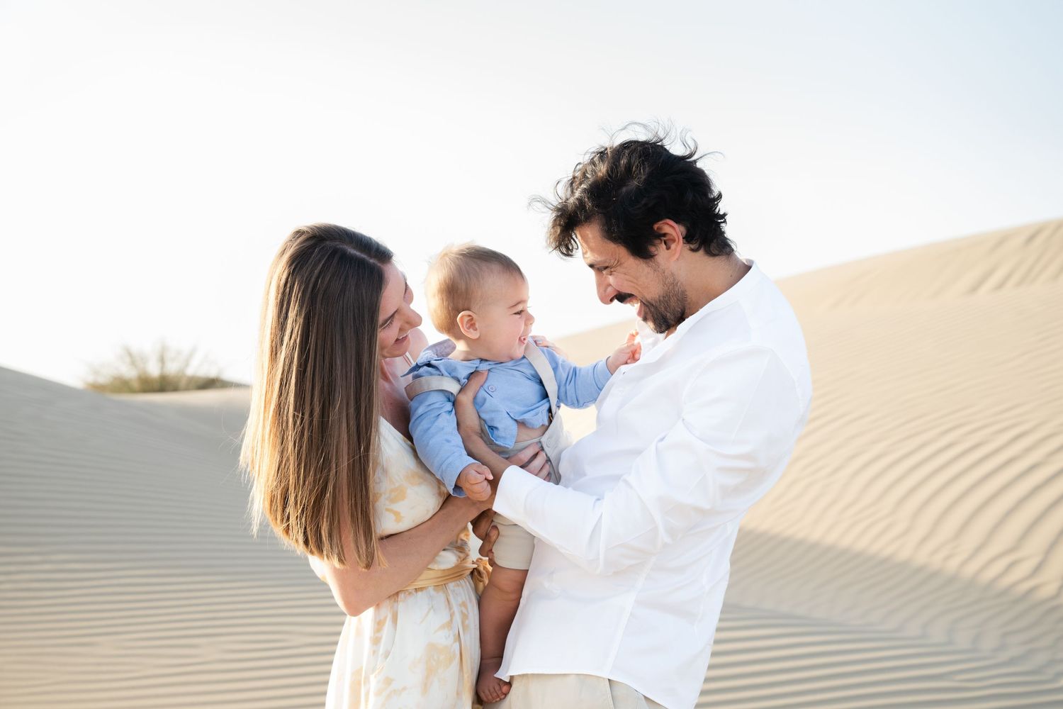 A family shares a joyful moment together while standing on sand dunes against a bright sky.