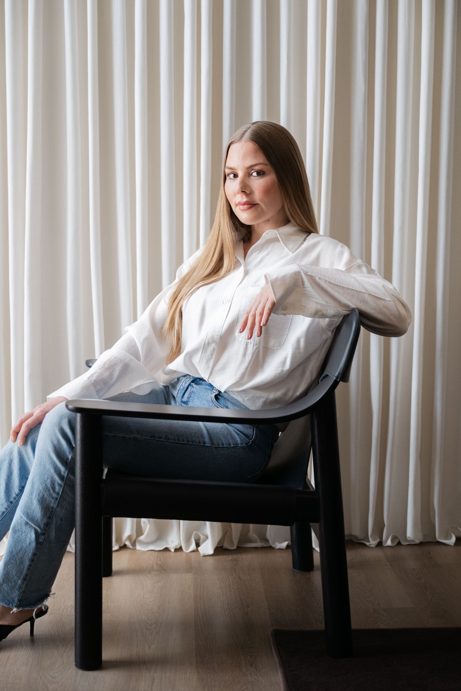 Minimalist portrait series on black chair against white curtain background.