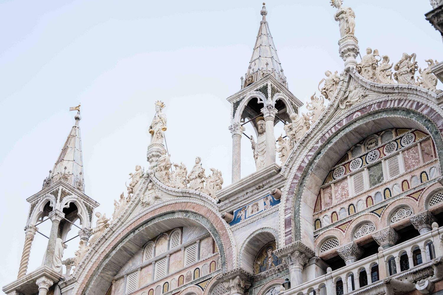 Ornate Gothic spires and architectural details of St. Mark's Basilica in Venice against a bright sky.