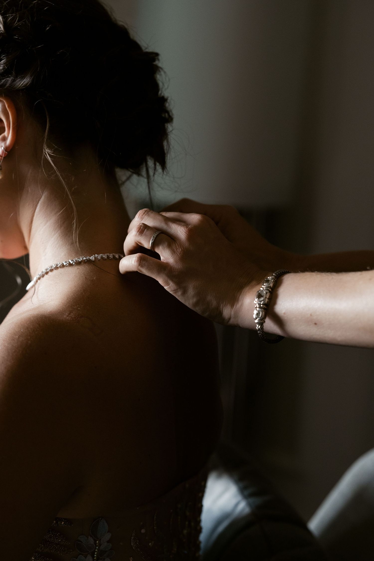 A delicate necklace being fastened around a neck in an intimate getting-ready moment.