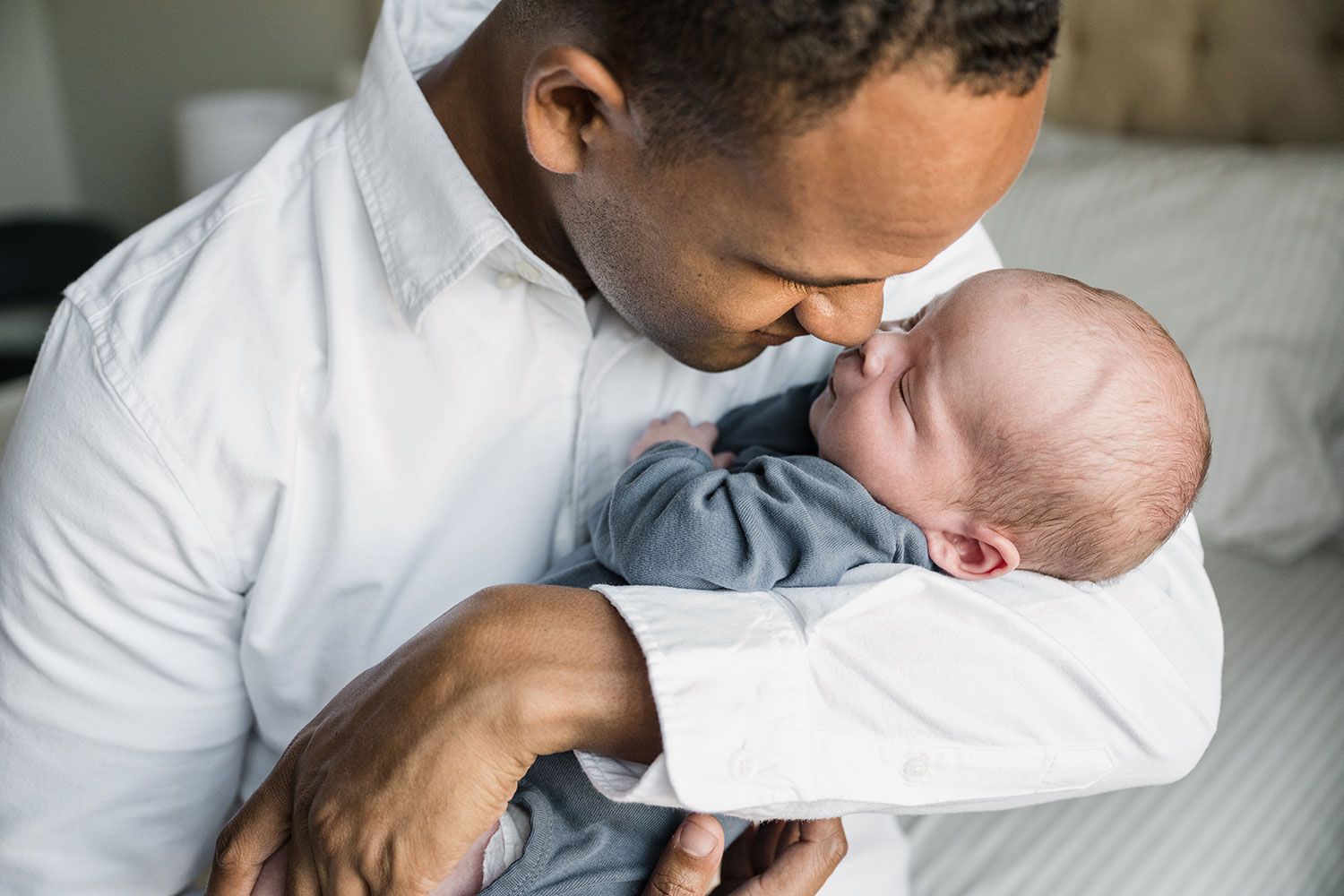 Parent lovingly kisses newborn baby while holding him in a tender embrace.