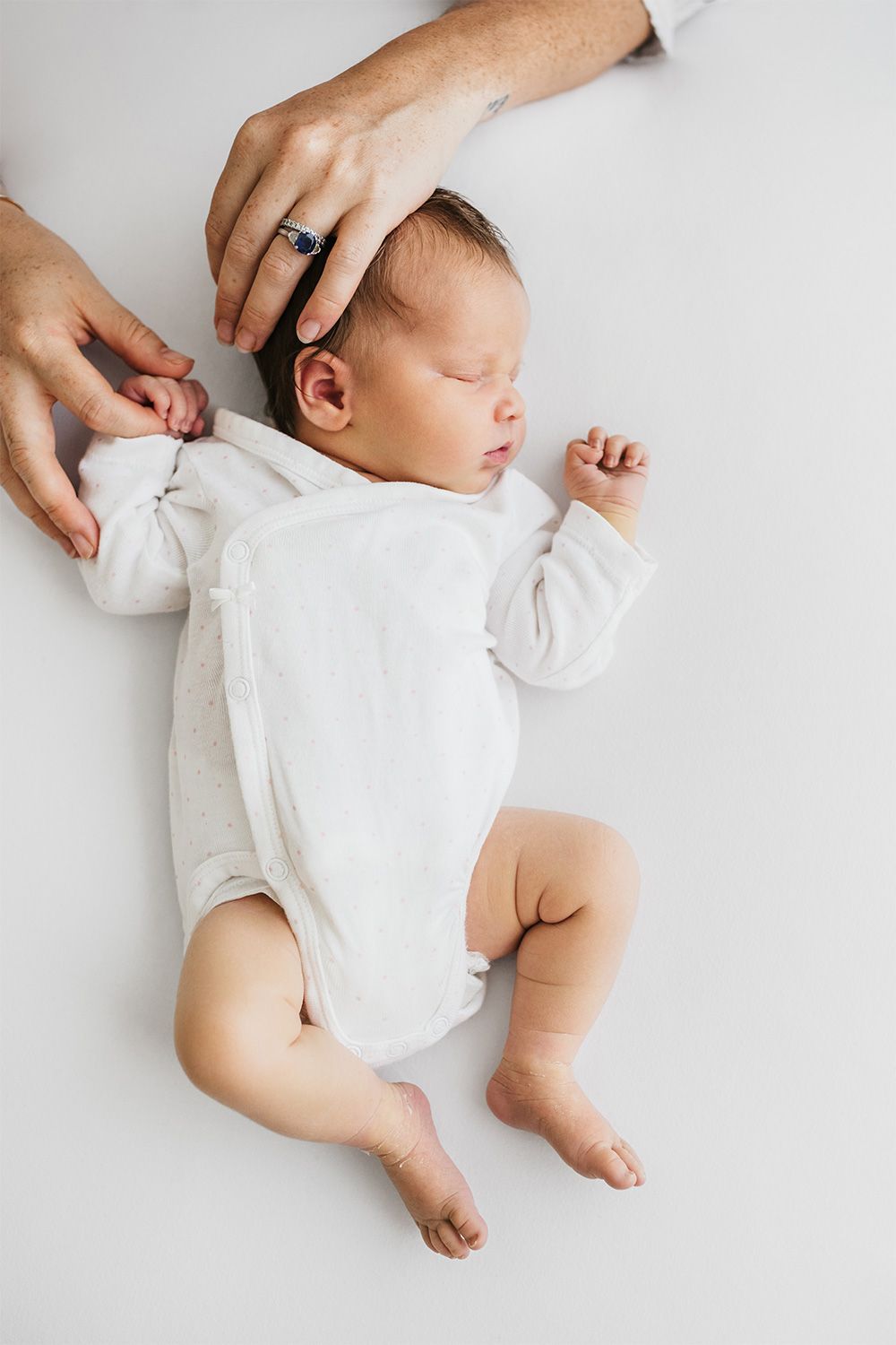 Sleeping baby in white onesie shown in four sequential poses on light background.