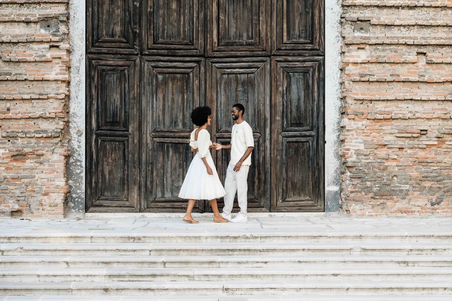 A couple stands together on stone steps before an antique wooden door.