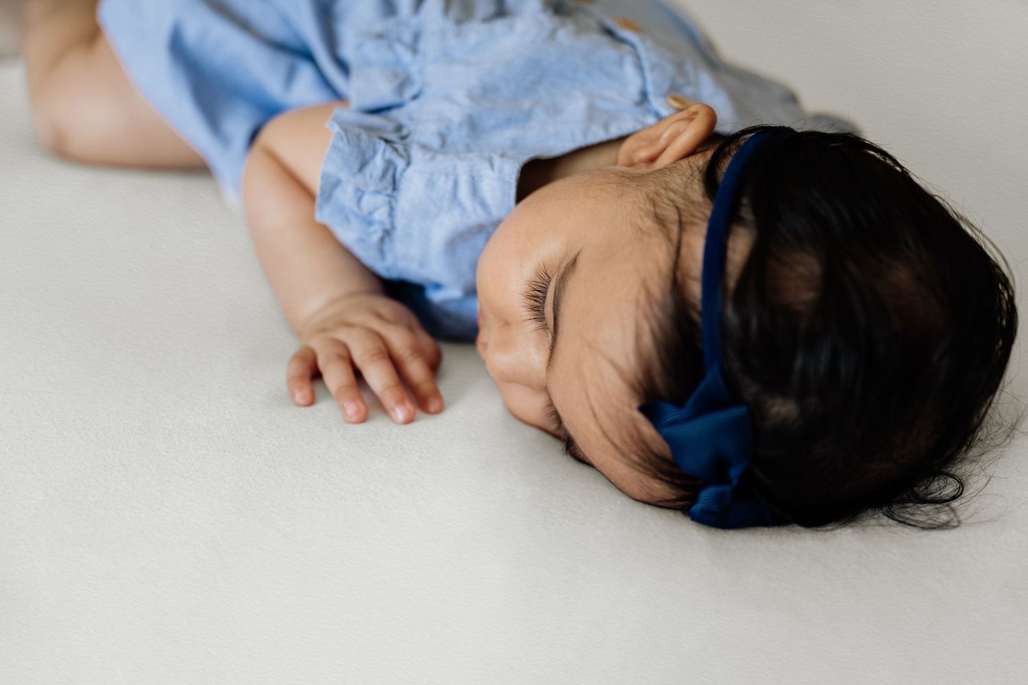 Baby in blue dress lying down during professional photo shoot on white backdrop.