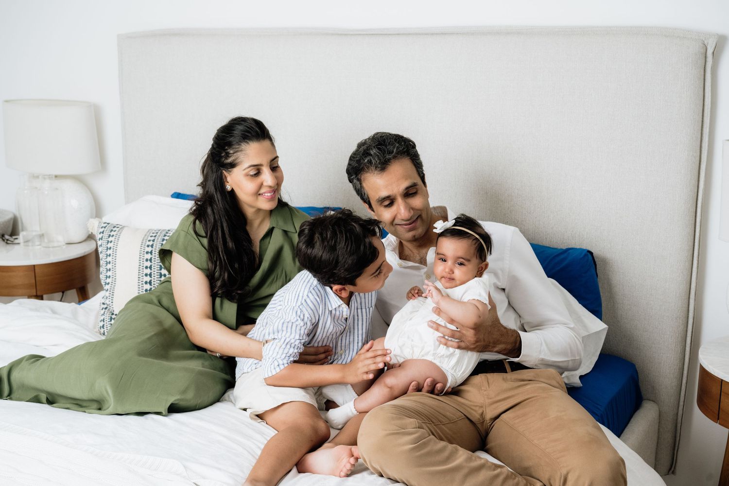 Family bonding time captured in a series of casual indoor photos on white bedding.