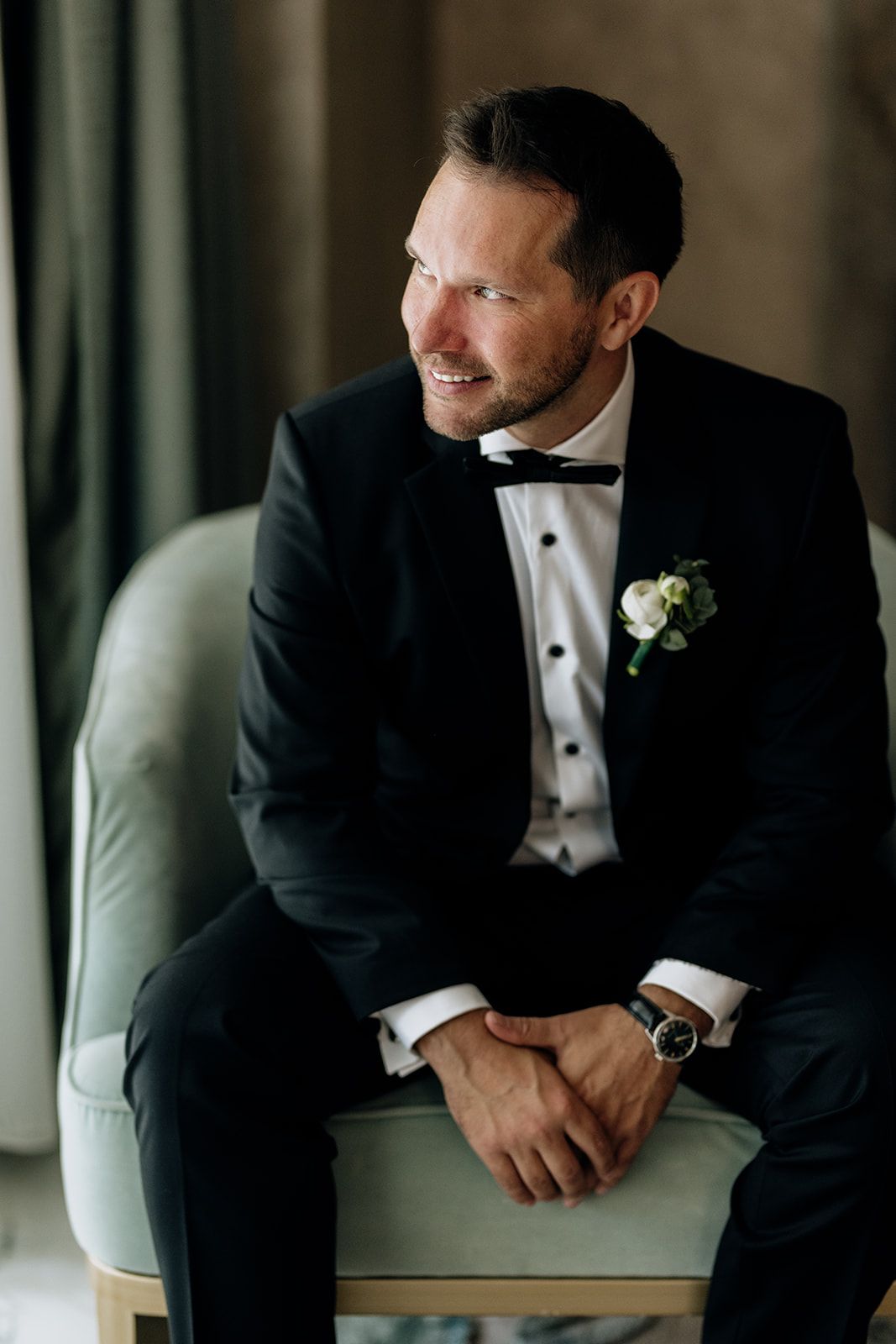 Groom in black tuxedo poses thoughtfully during wedding portraits.