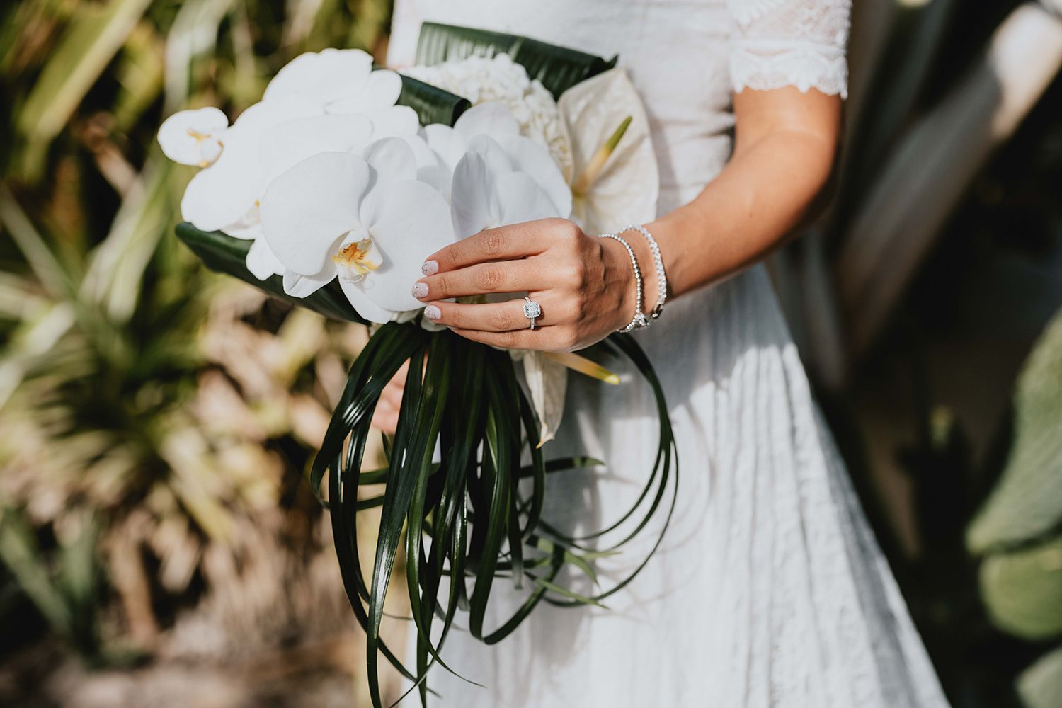White orchid bridal bouquet with trailing greenery held against a lace wedding dress.