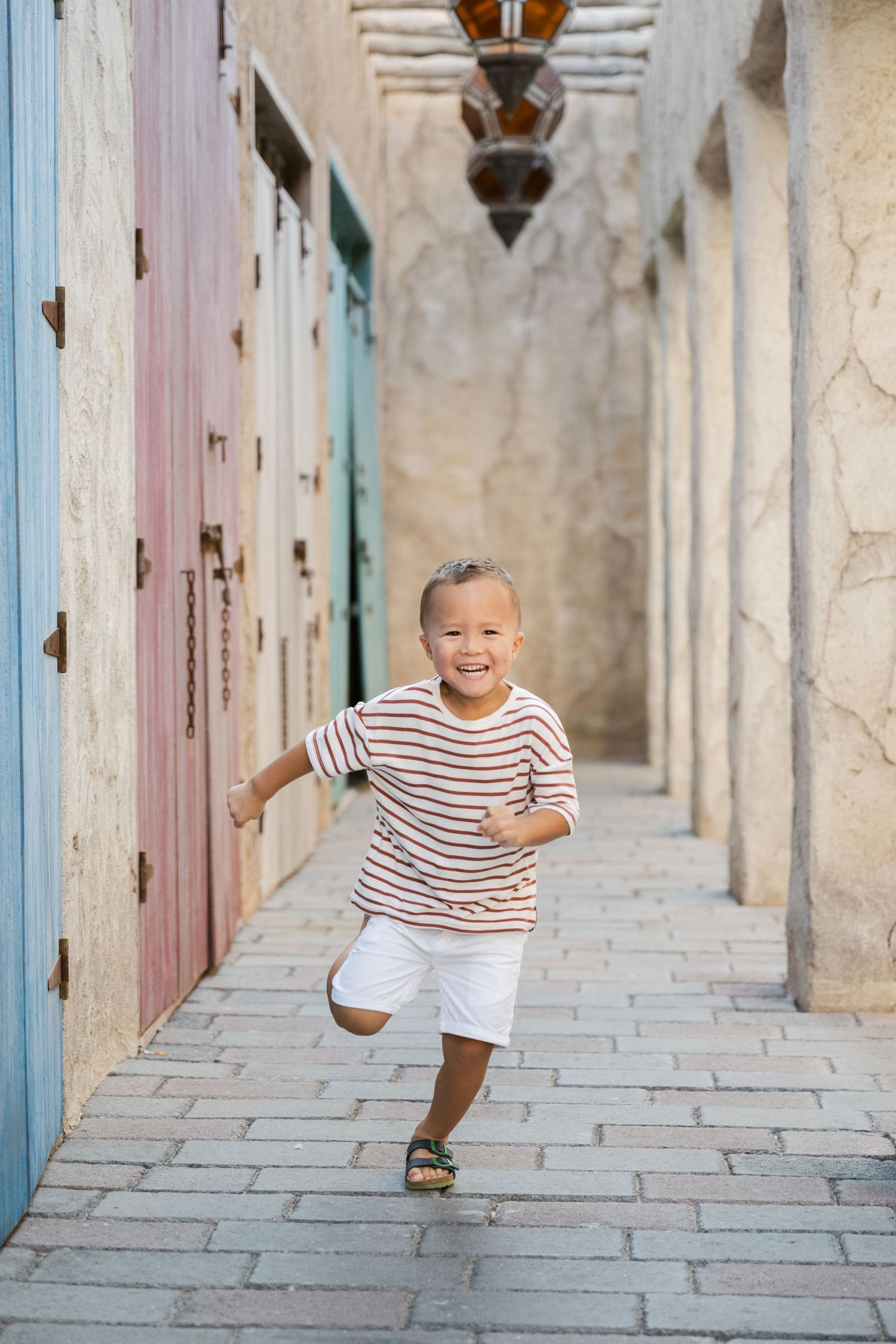 Child in striped shirt running playfully through a corridor with colorful doors.