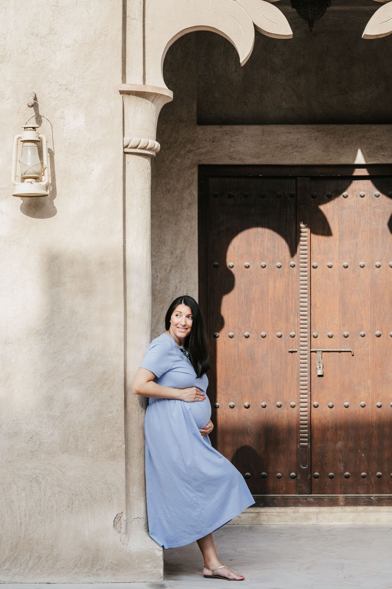 Maternity photos against traditional wooden door and stone archway in Middle Eastern setting.