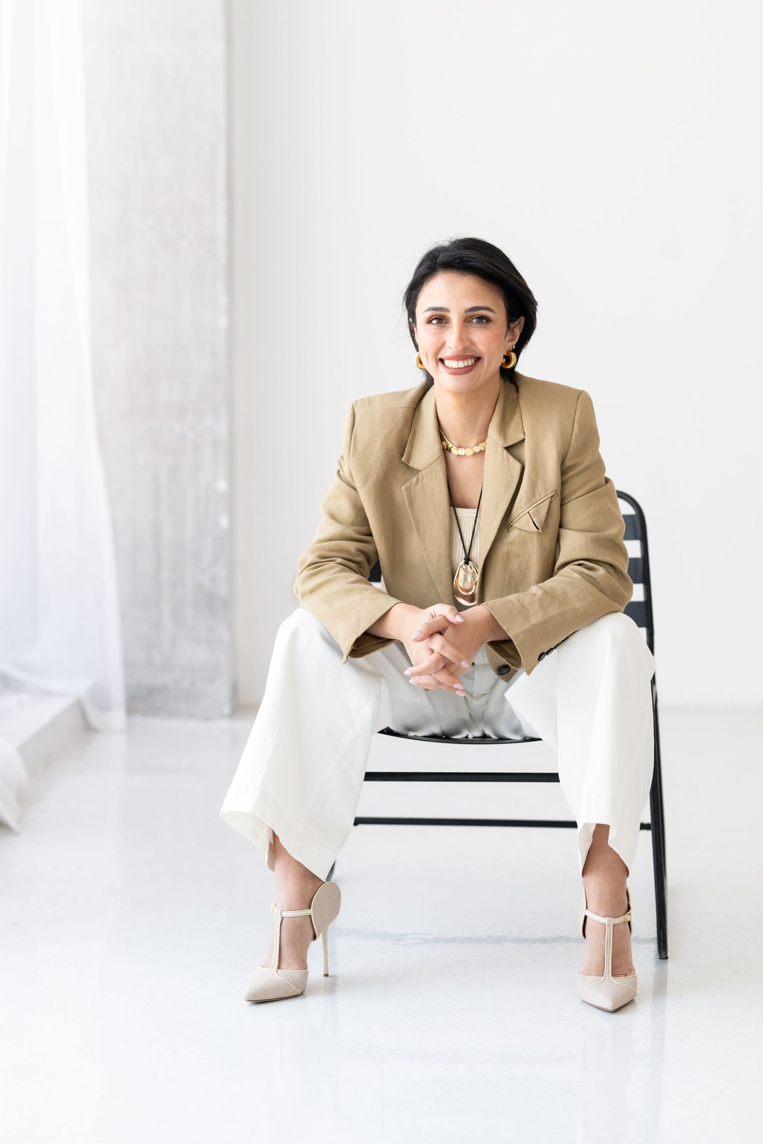 Professional in beige blazer seated in minimalist white office setting.