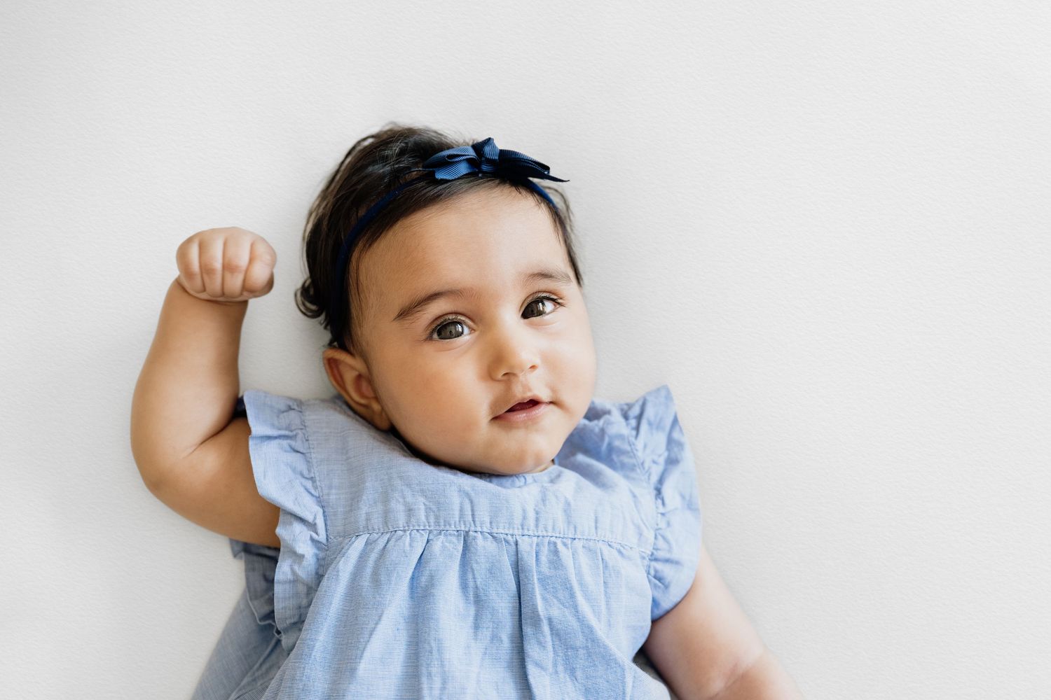 Baby in ruffled blue dress smiling during professional photo session.