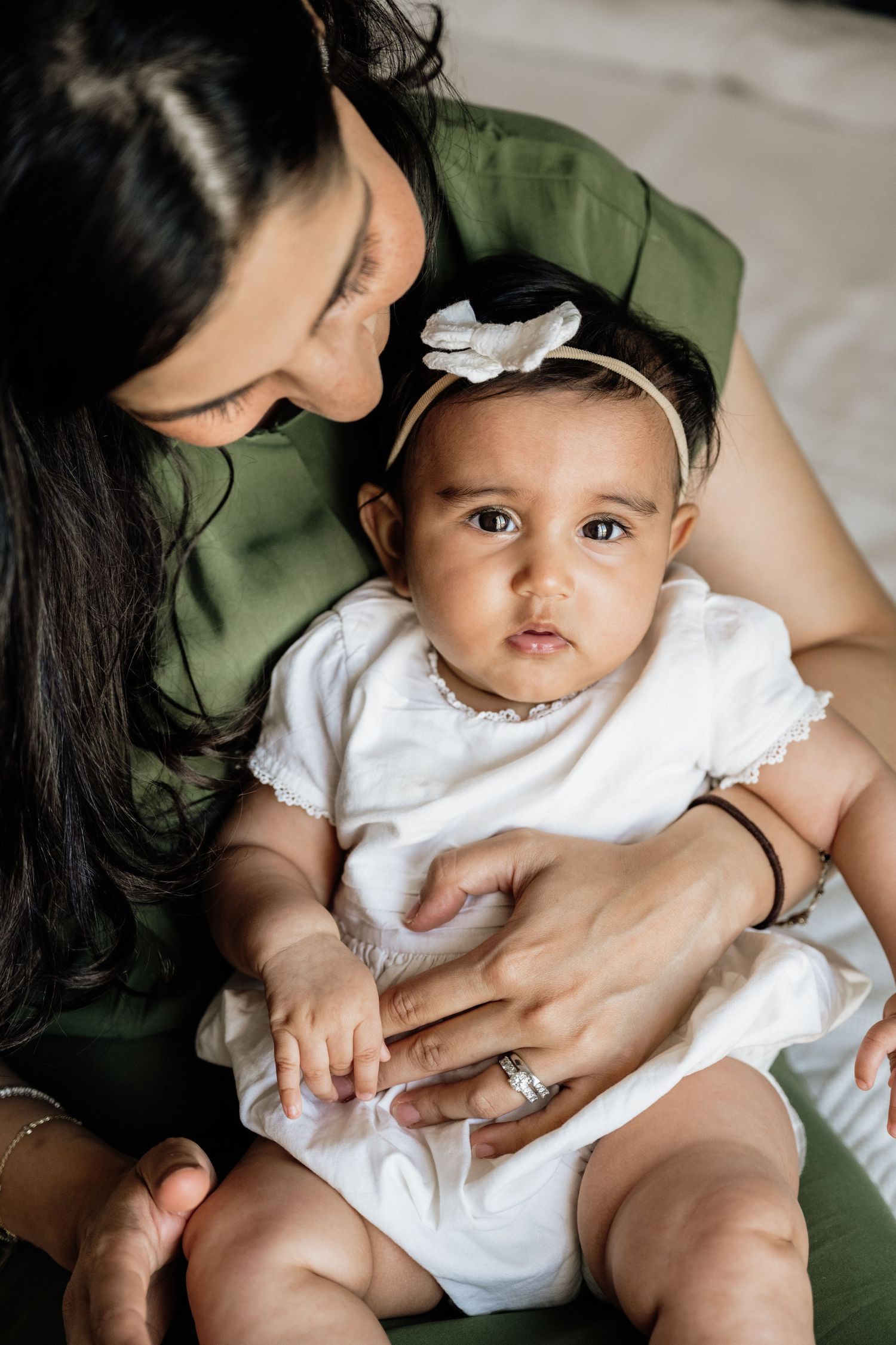 Intimate family photoshoot featuring baby in white dress with bow headband.