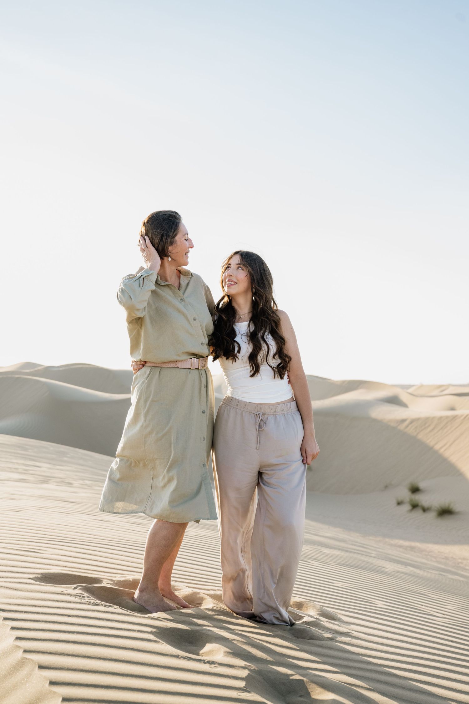 A couple shares intimate moments while walking together on sand dunes during a desert photoshoot.
