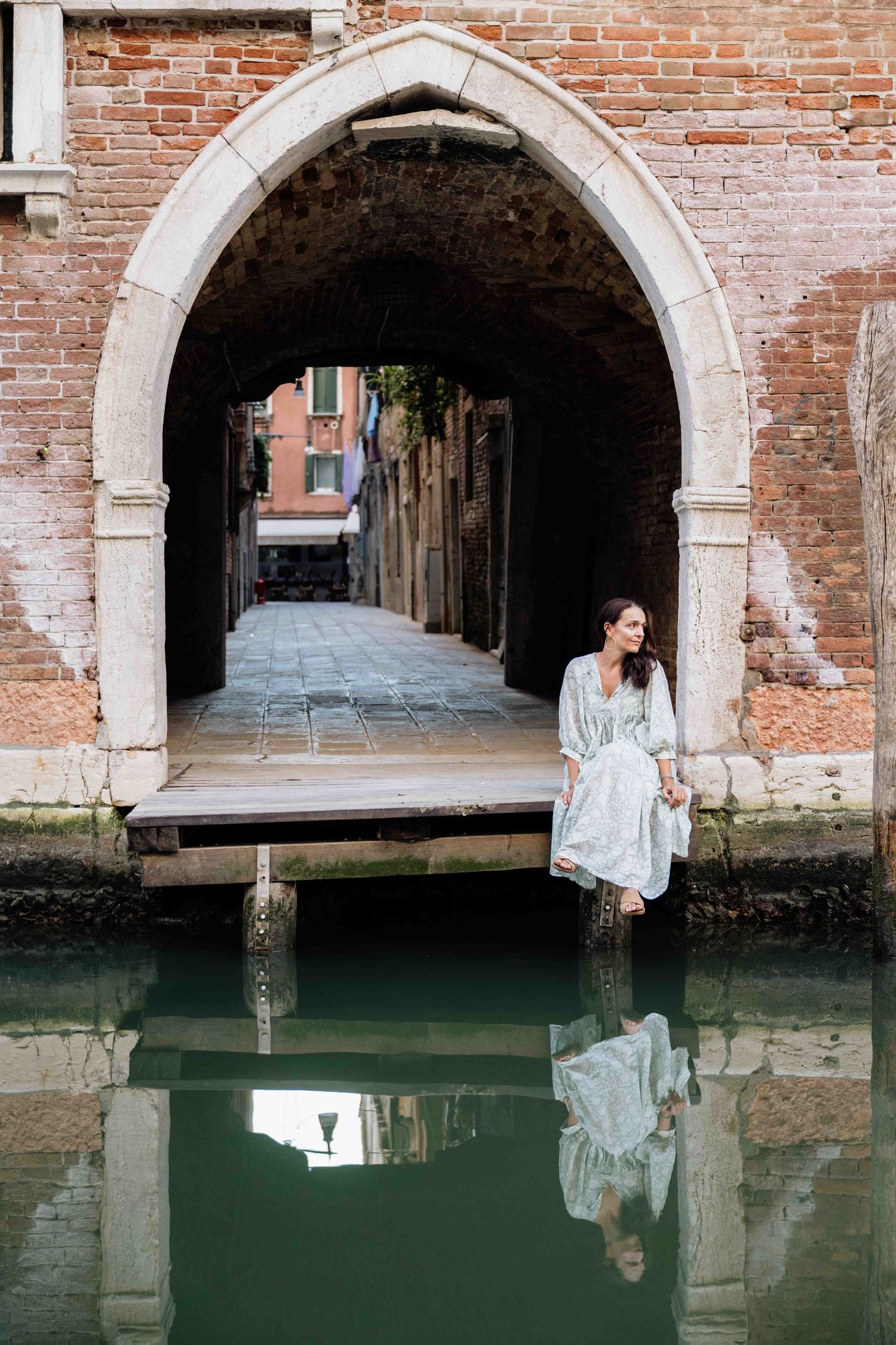 Fashion shoot by Venetian canal with brick archways reflecting in green water.