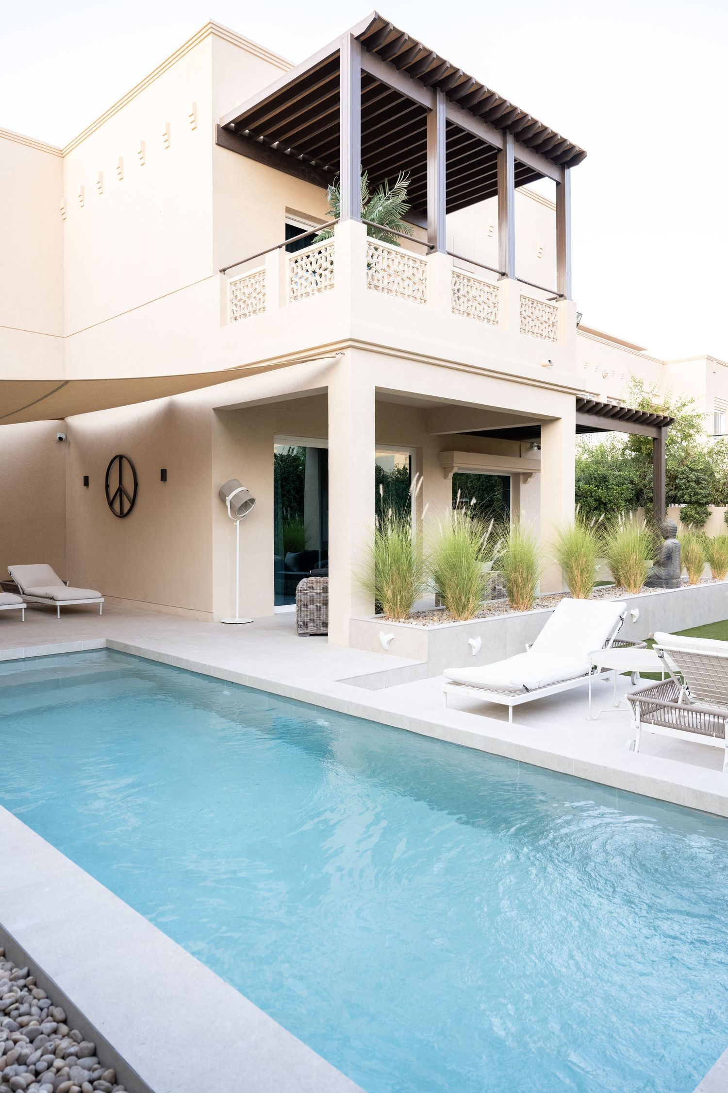 Luxury villa exterior with swimming pool and modern lounge chairs in desert landscape.
