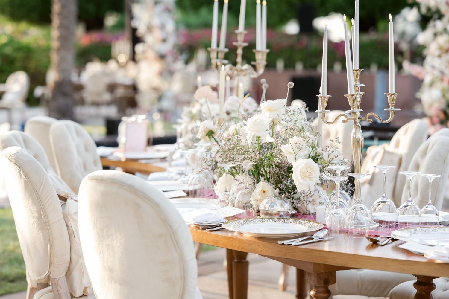 Elegant table setting with white chairs, tall candles, and delicate floral centerpieces.
