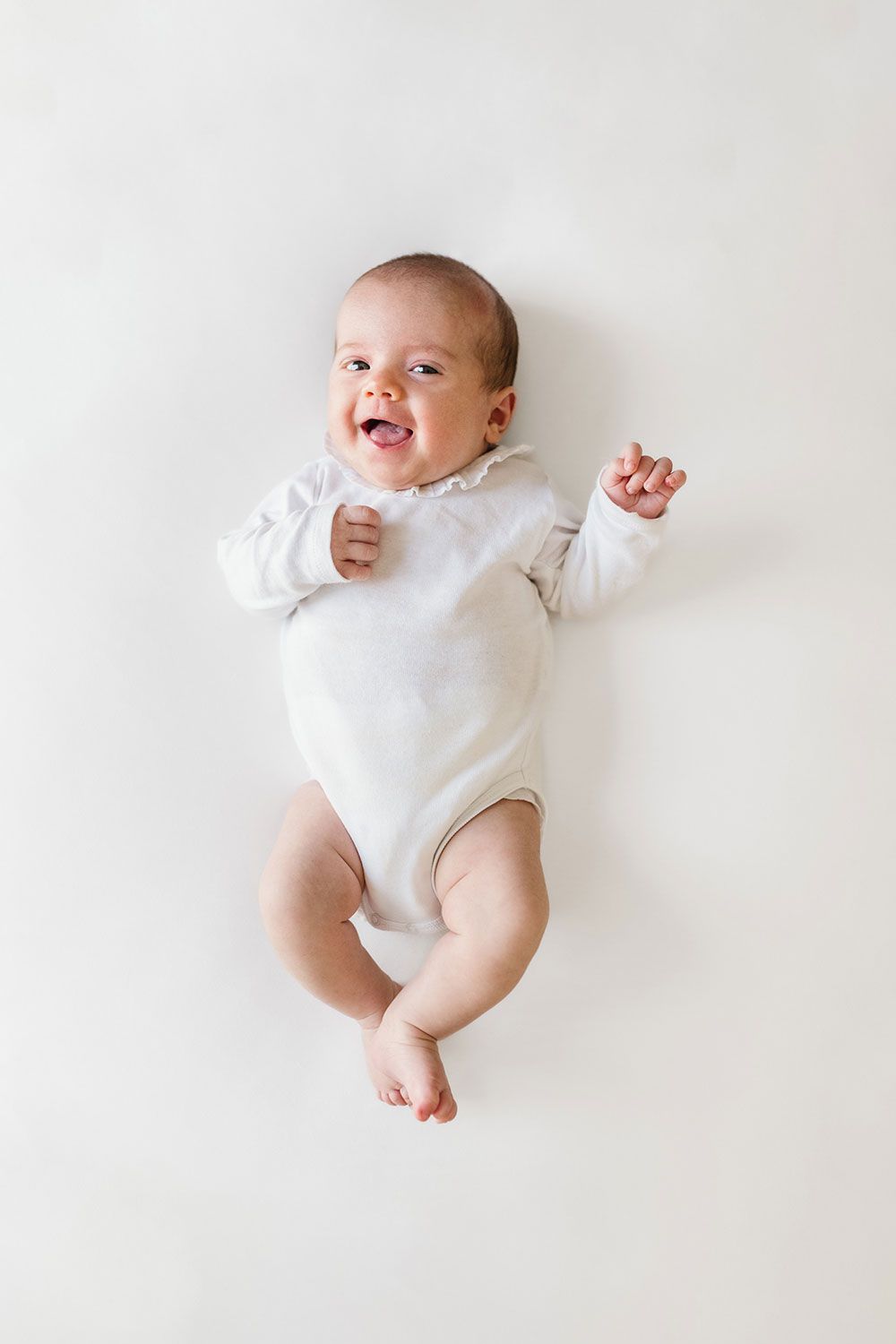 A happy baby wearing a white onesie lies on a white background in a series of playful poses.