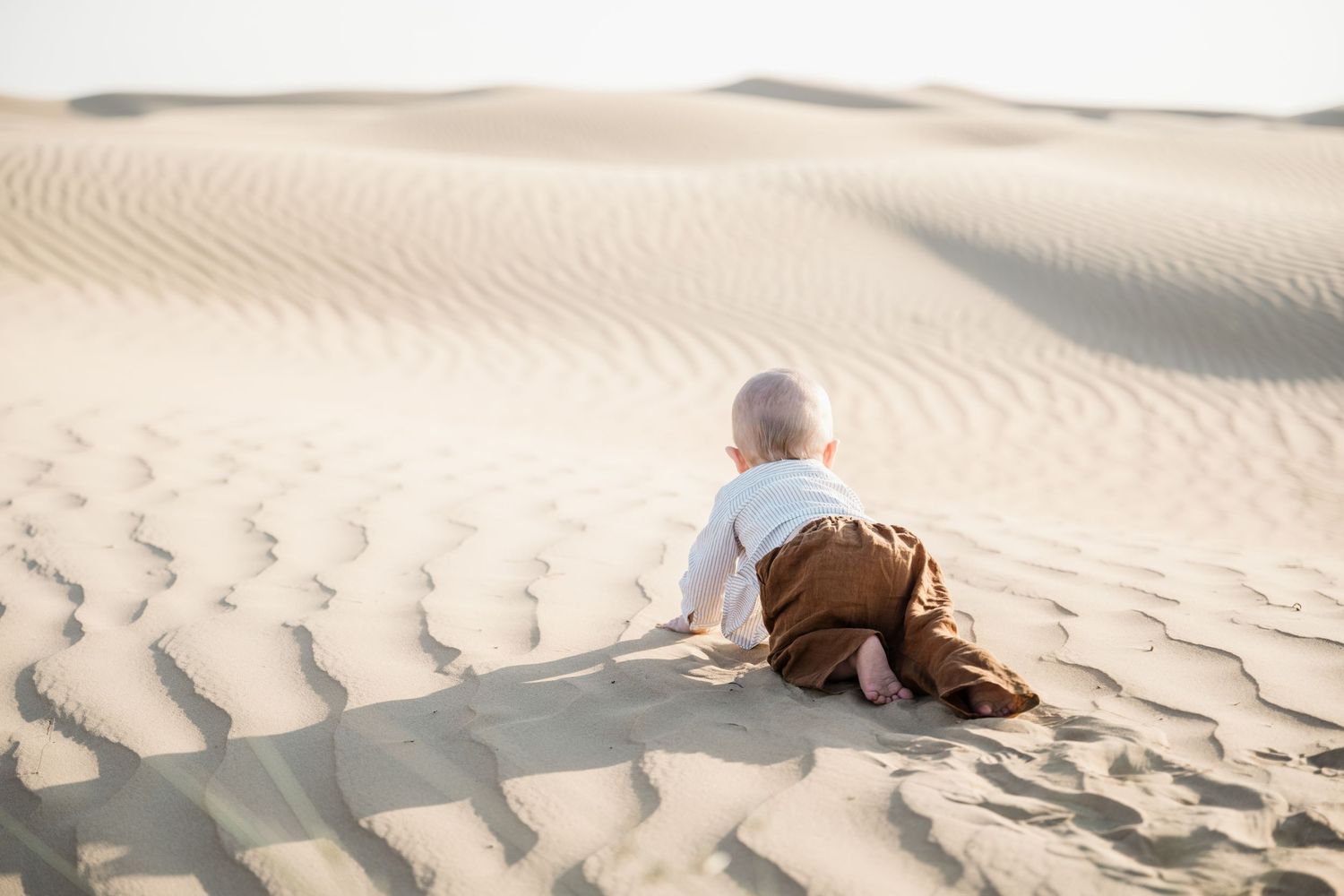 Small child sitting alone on textured desert sand during golden hour.