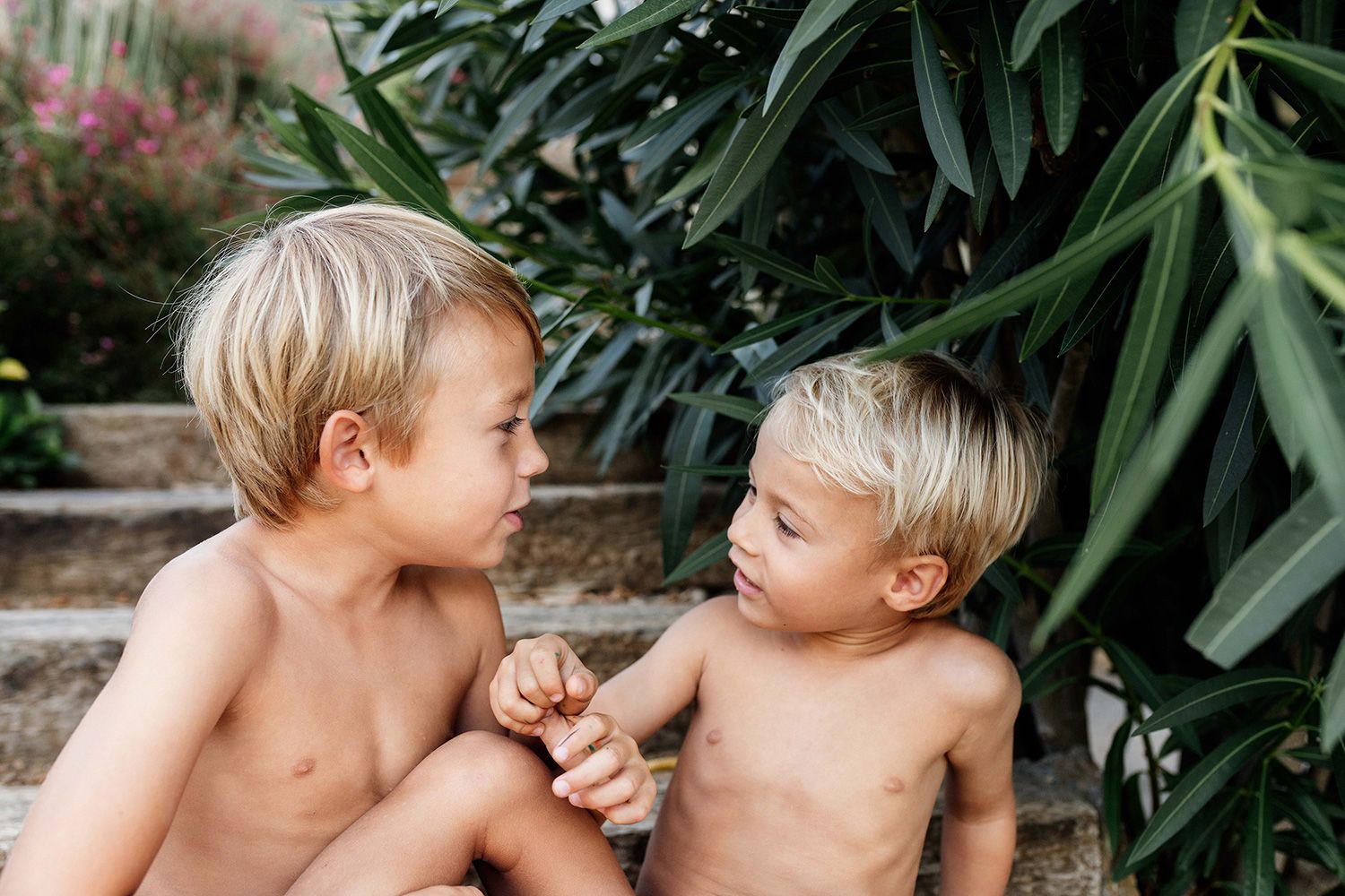 Two young children share a tender moment while playing outdoors surrounded by lush greenery.