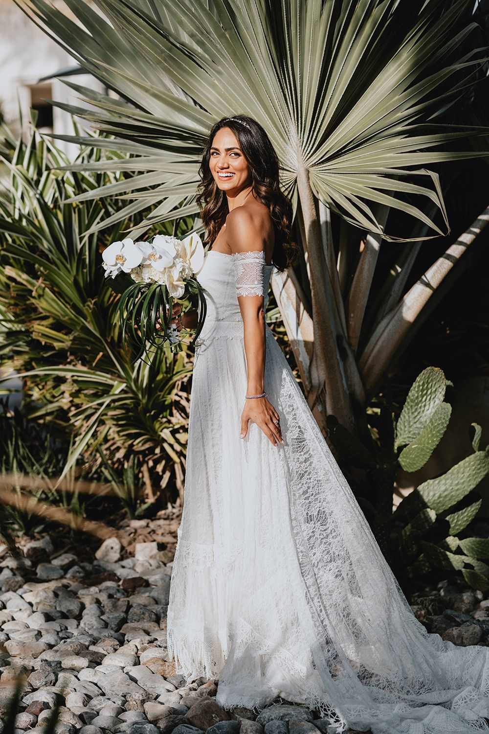 Elegant off-shoulder wedding dress photographed in a tropical garden setting.