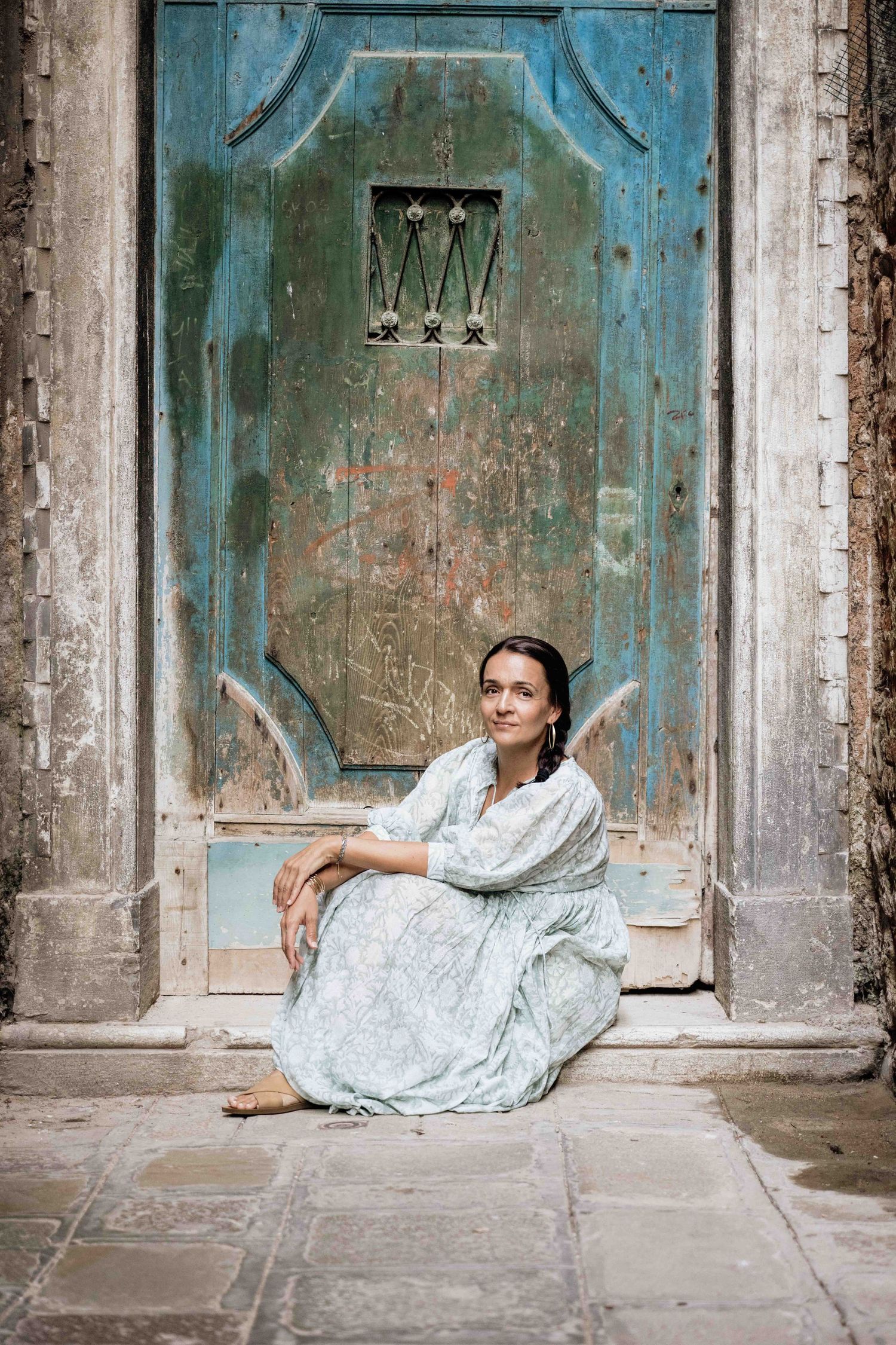 Artistic fashion poses against historic Venetian doorway with peeling turquoise paint.