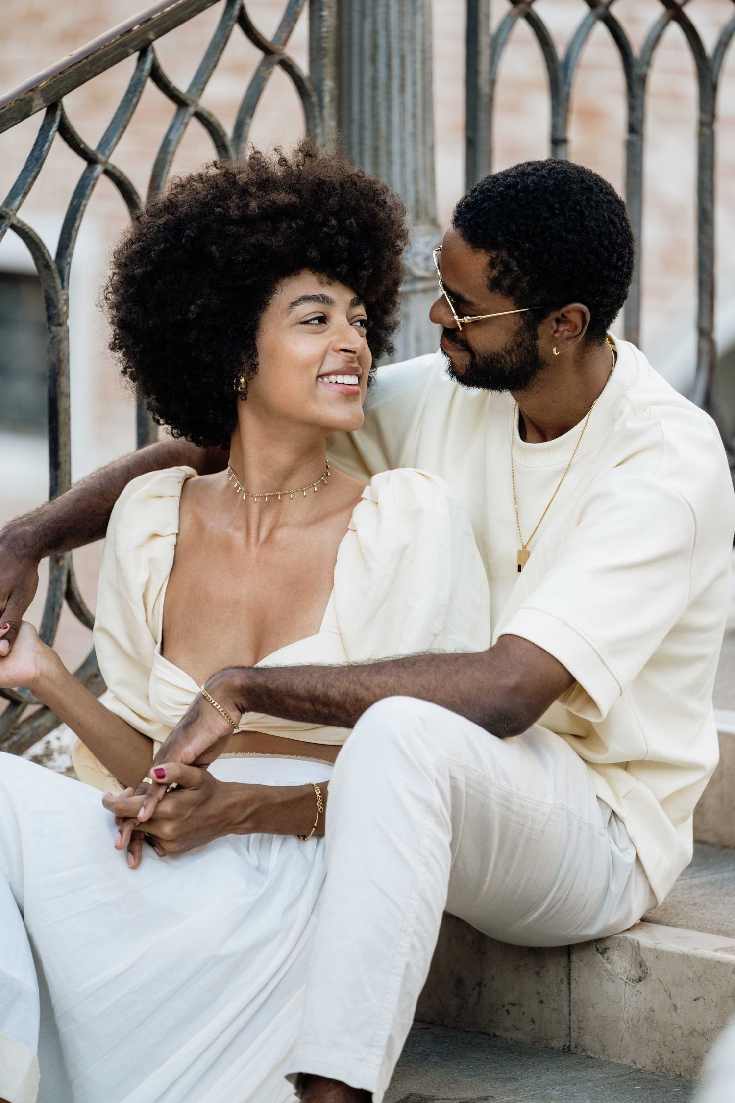 Couple in white outfits shares intimate moments on ornate iron railing.