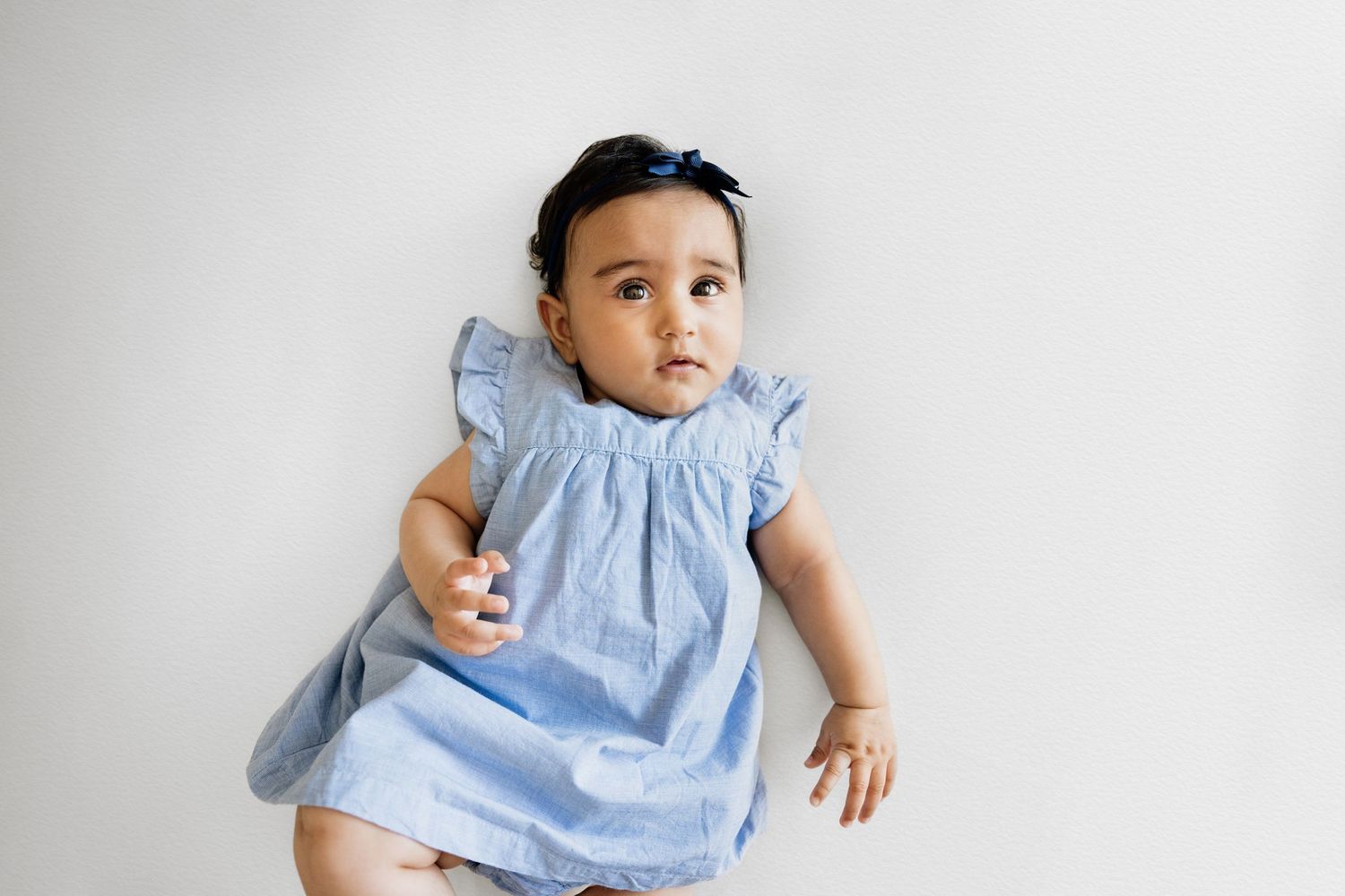 Baby wearing light blue dress lying on white background during photo session.