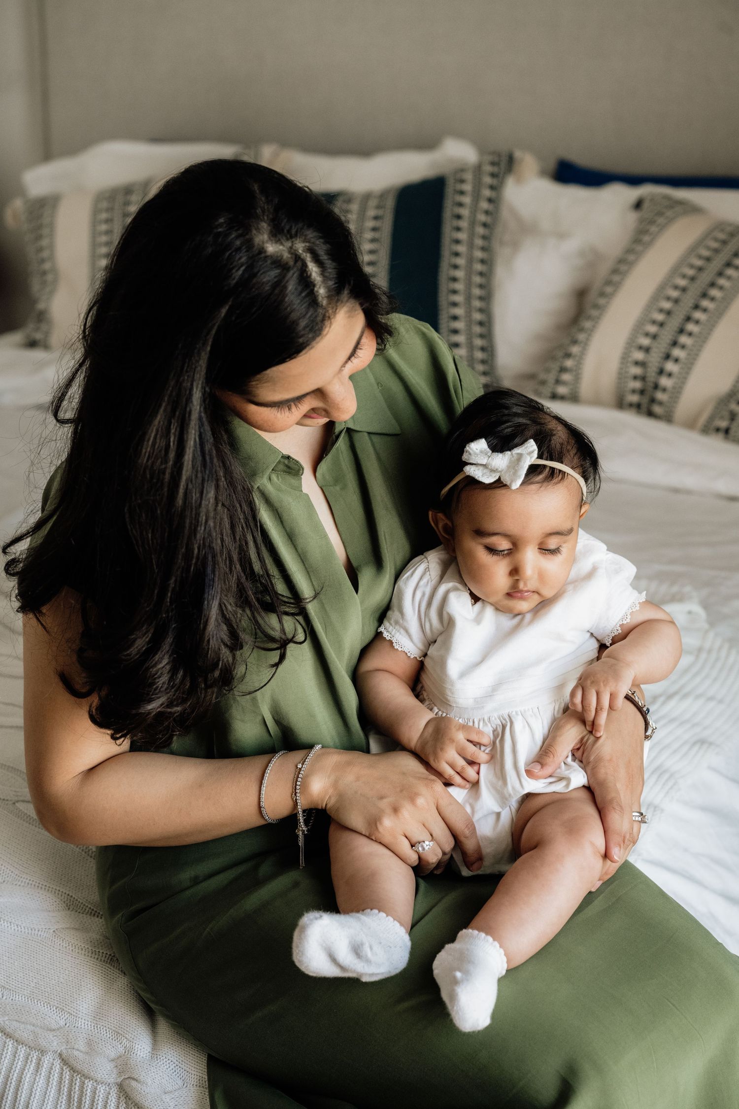 Tender moments between parent and infant wearing white on a cozy bed with decorative pillows.