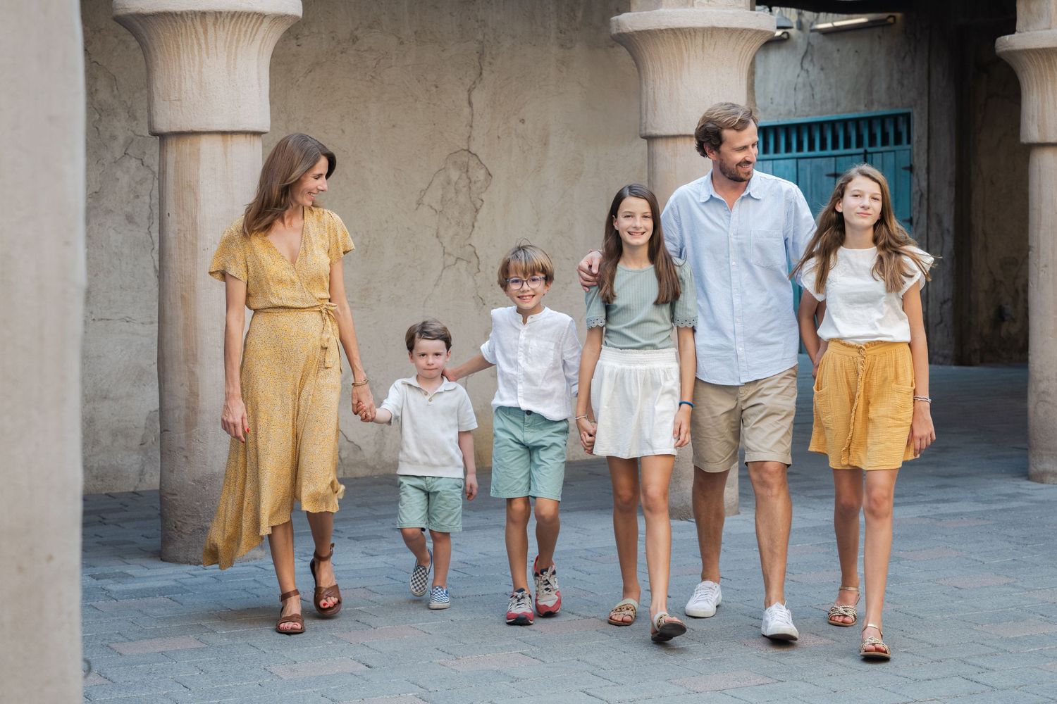 A family walks together through a stone archway wearing coordinated light colored outfits.