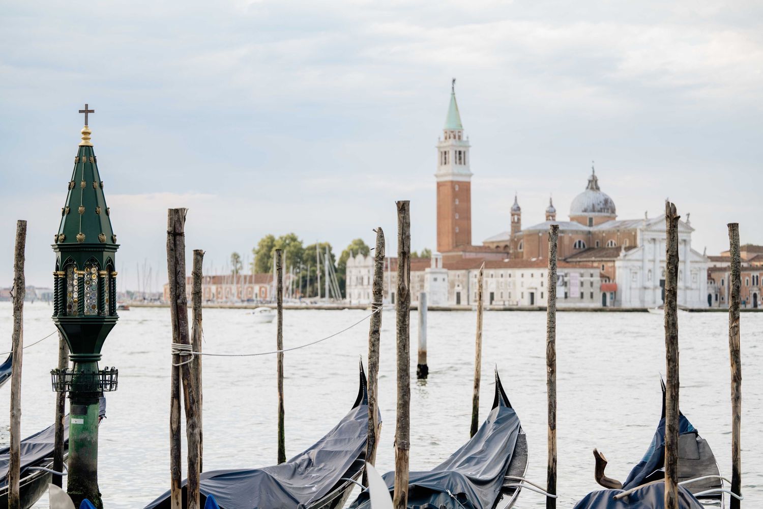 Traditional Venetian gondolas and mooring posts silhouetted against the lagoon and distant buildings.
