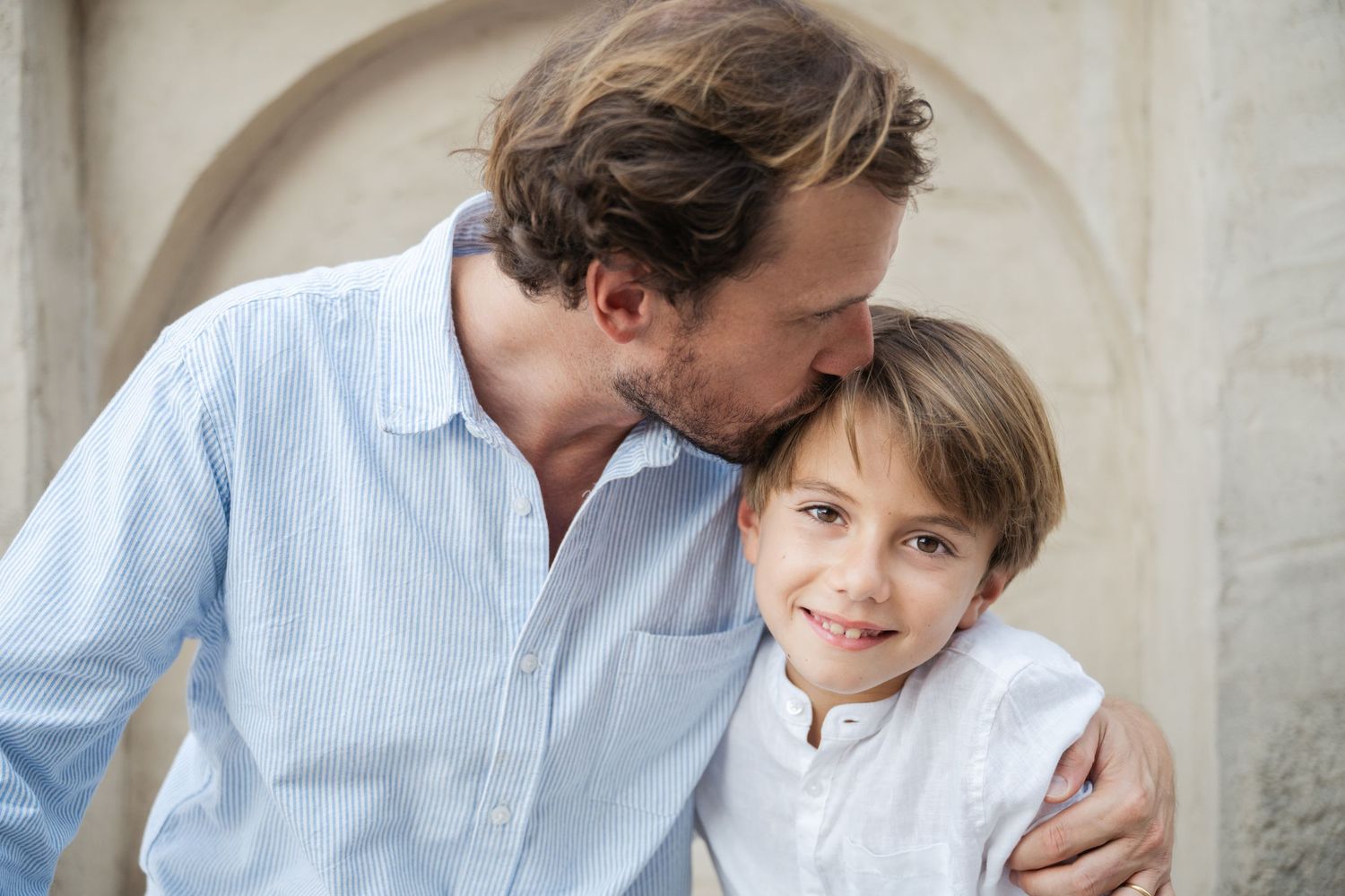 Intimate family moment captured against light colored wall with natural lighting.
