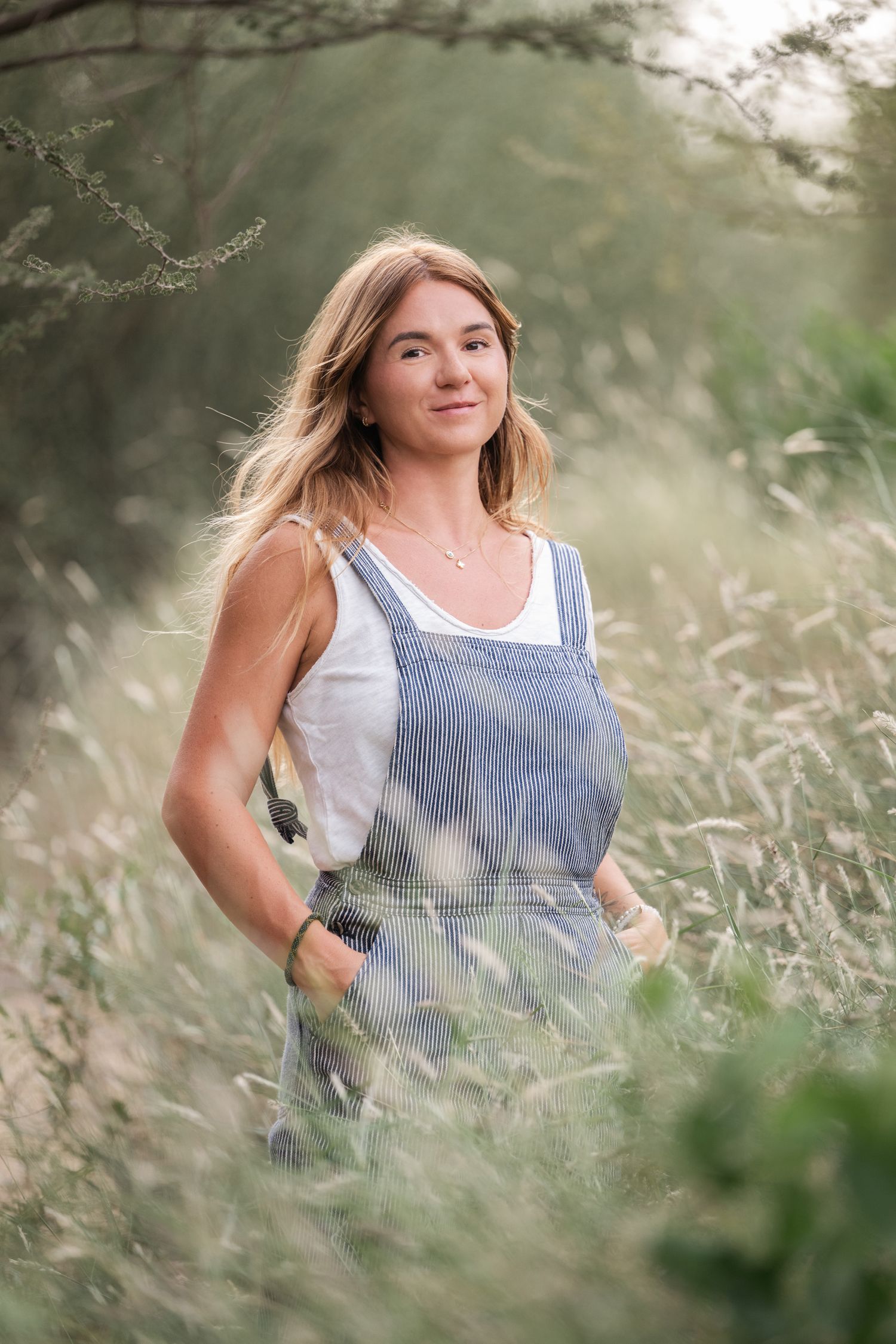 A person in a blue and white striped tank top stands among tall grass in a dreamy outdoor setting.