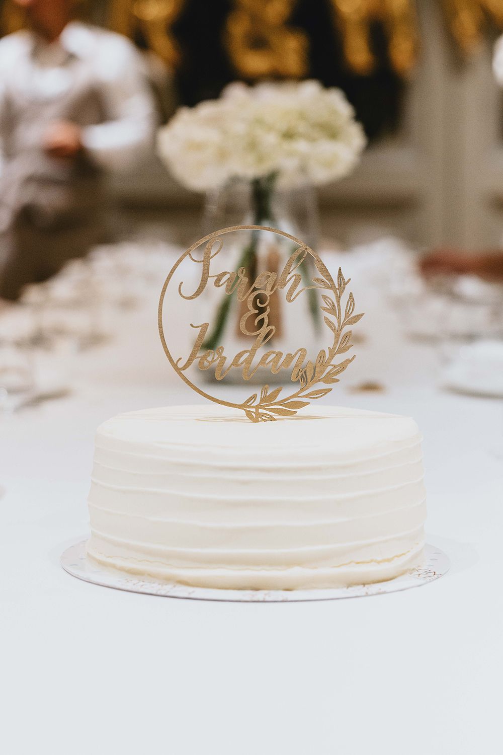 Elegant white wedding cake with gold decorative toppers on a white tablecloth.