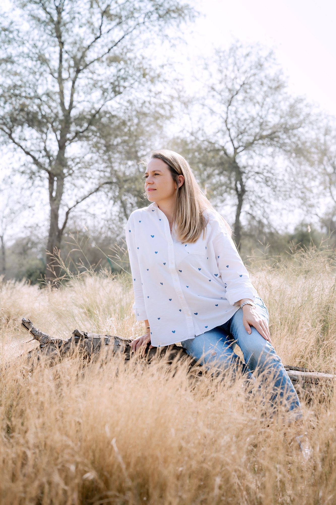 A person in a white sweater sits in a golden autumn field of tall grass during a serene outdoor photoshoot.