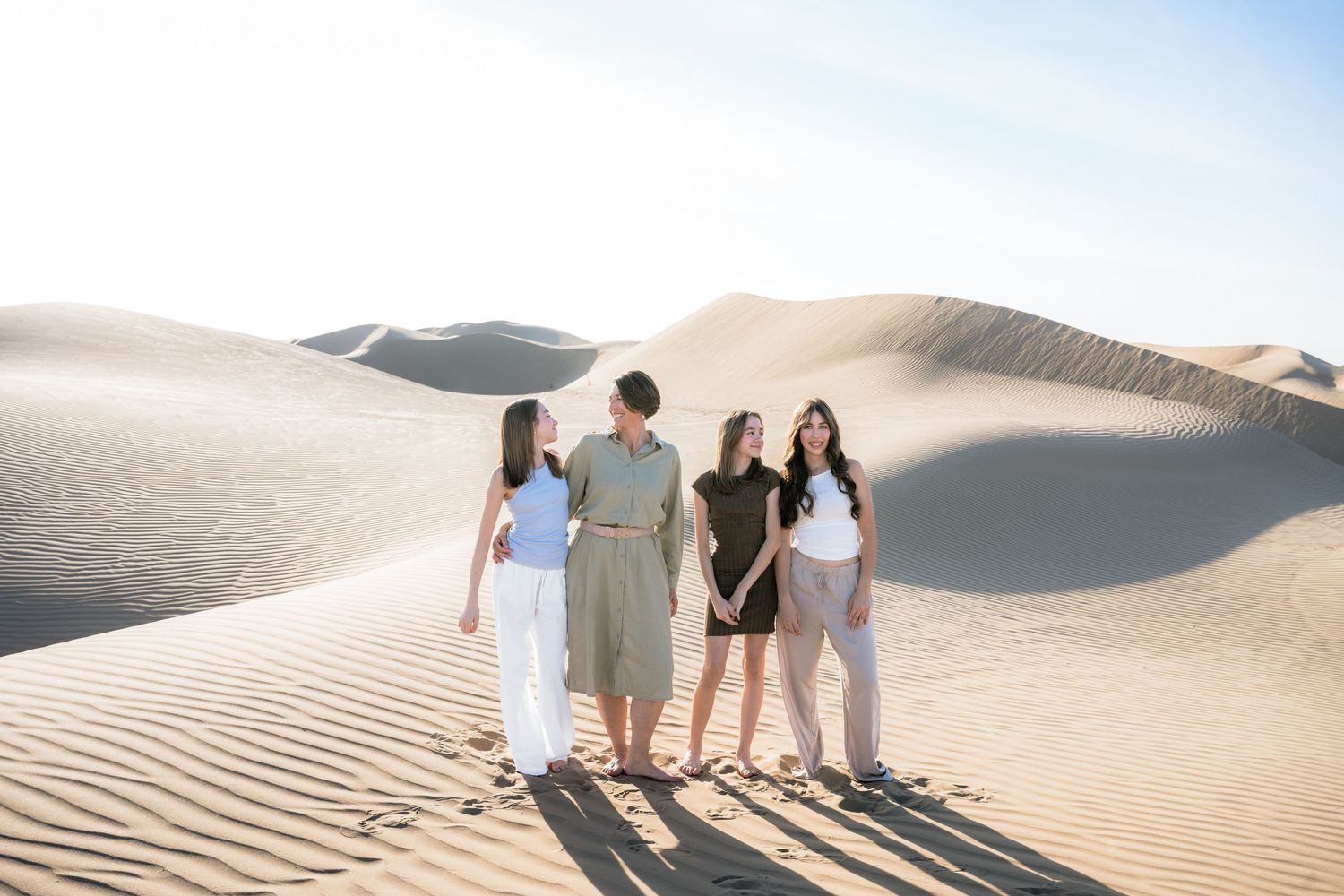 People walking along the crest of sand dunes against a bright blue sky.