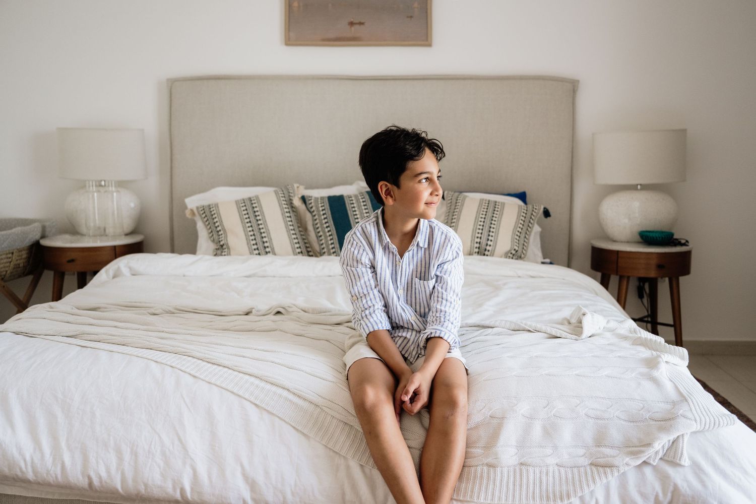 Wide panoramic shot of child sitting alone on large white bed.