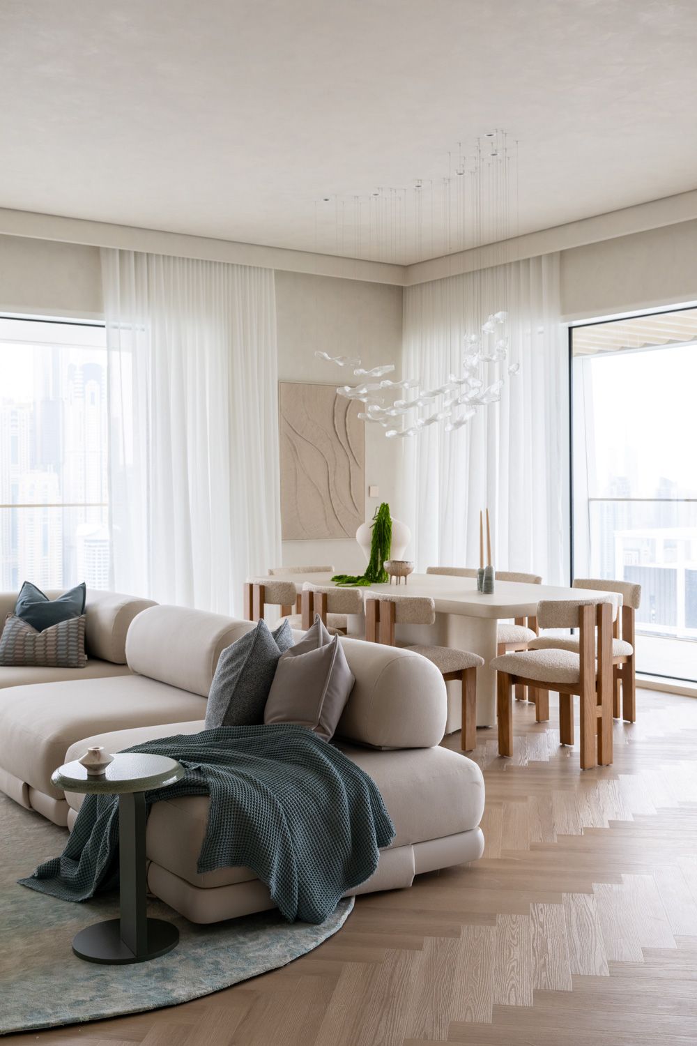 Modern minimalist living room interior with curved sofa, round rug and floor-to-ceiling windows in neutral tones.