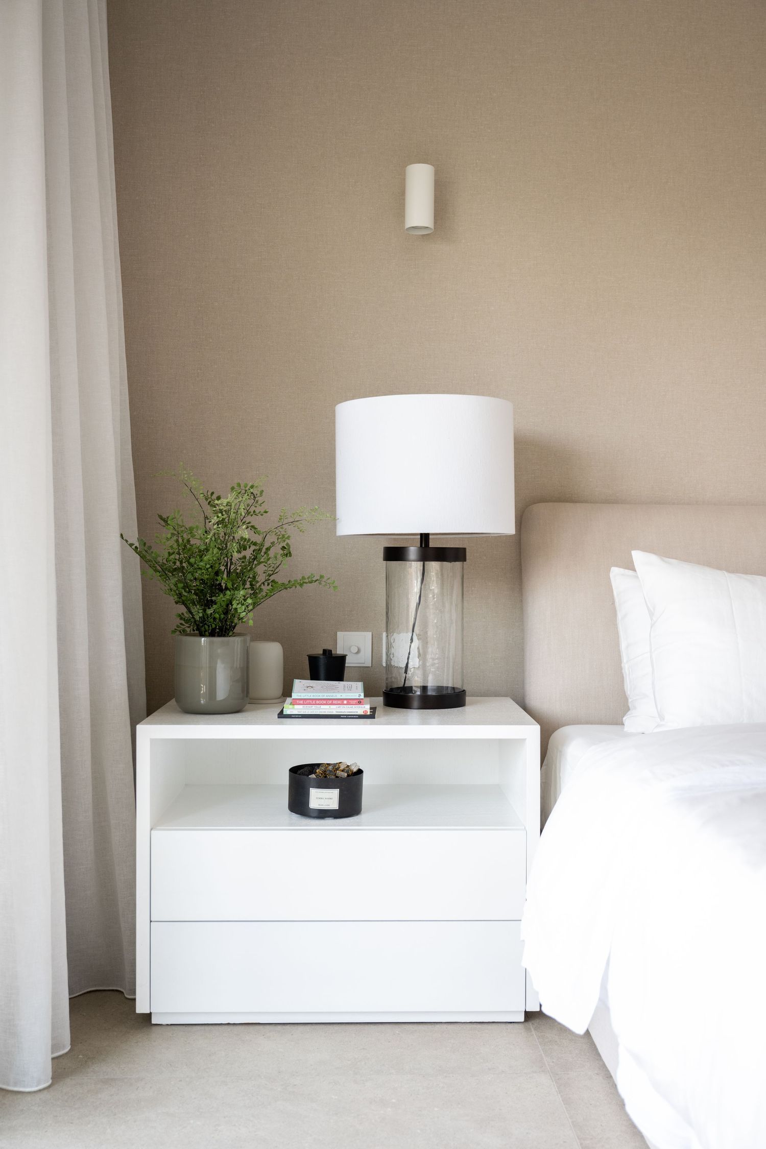 Minimalist bedroom interior with white furniture and subtle green plant accents.