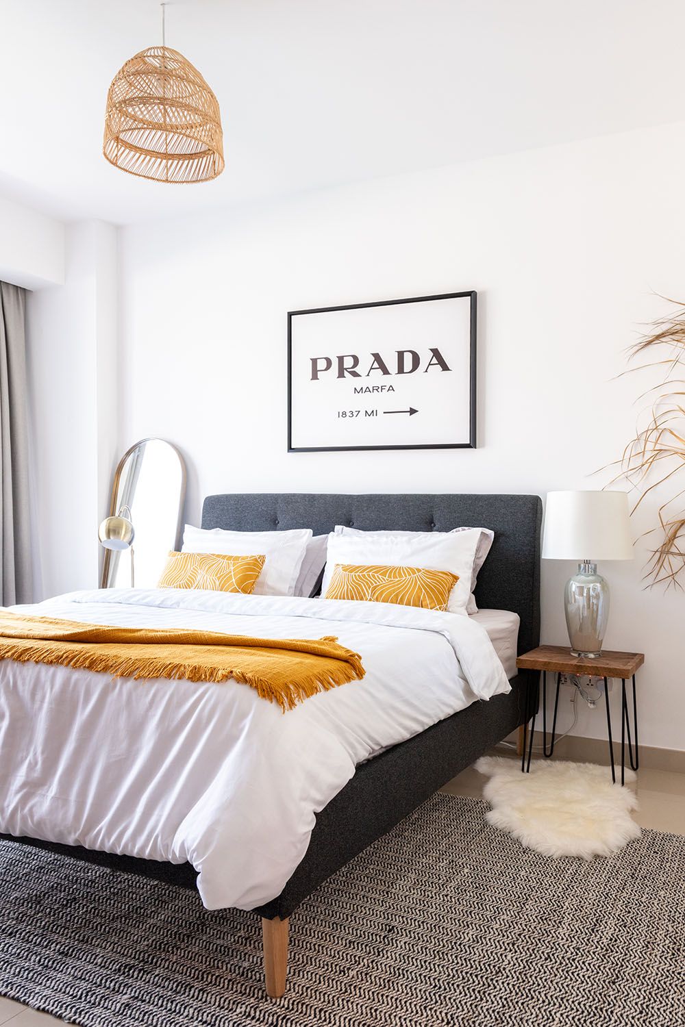 Modern bedroom with Prada artwork, rattan pendant light, and mustard yellow bedding accents.
