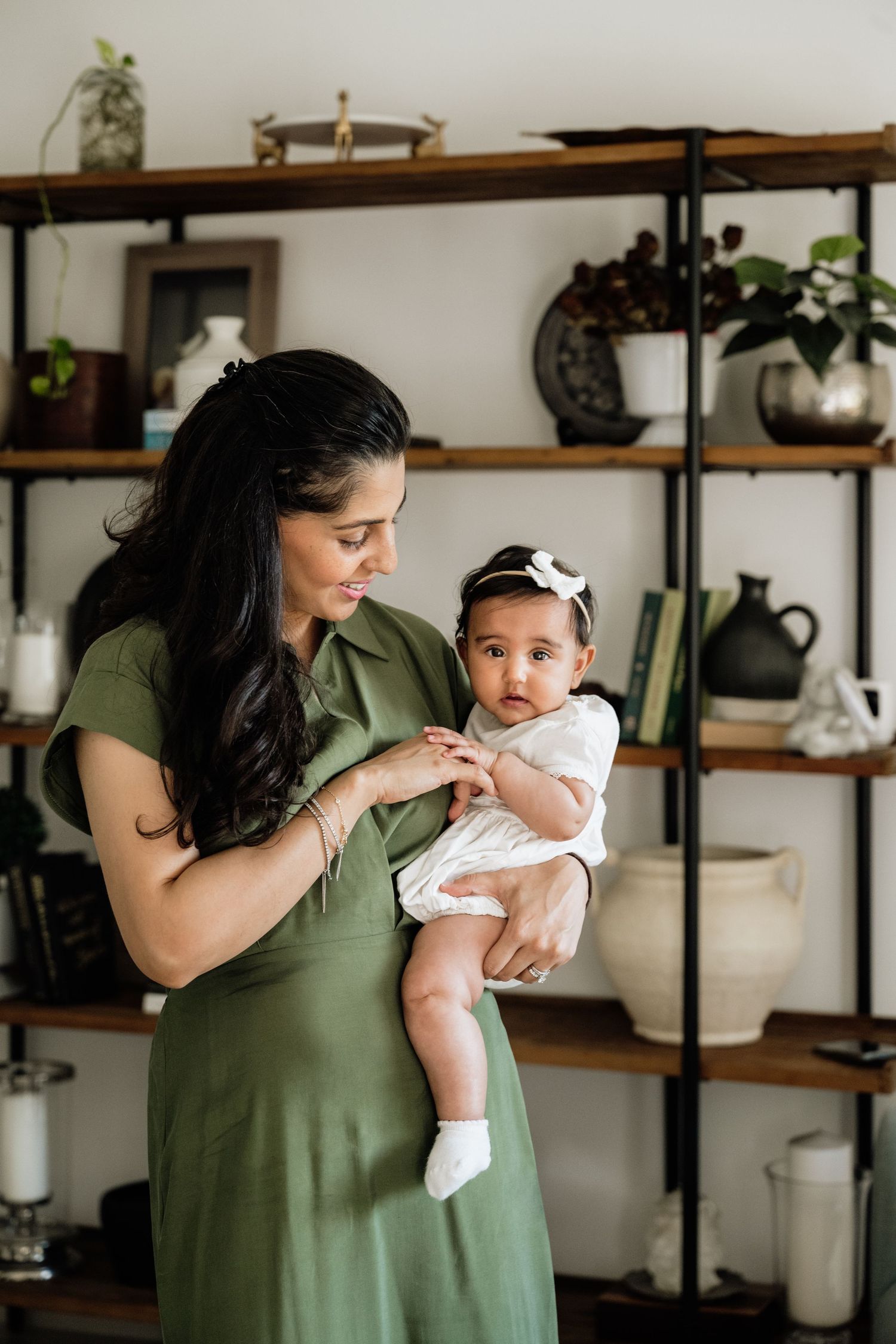 A tender moment between parent and infant in a modern home with wooden shelving and plants.