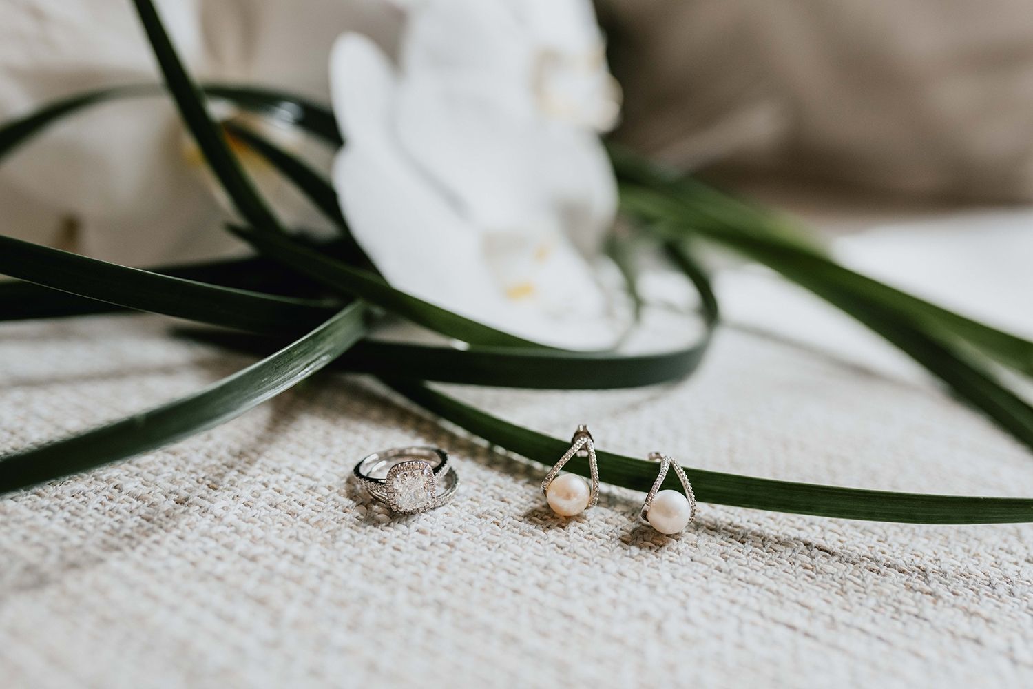 White orchids and greenery arranged with wedding rings on textured fabric.