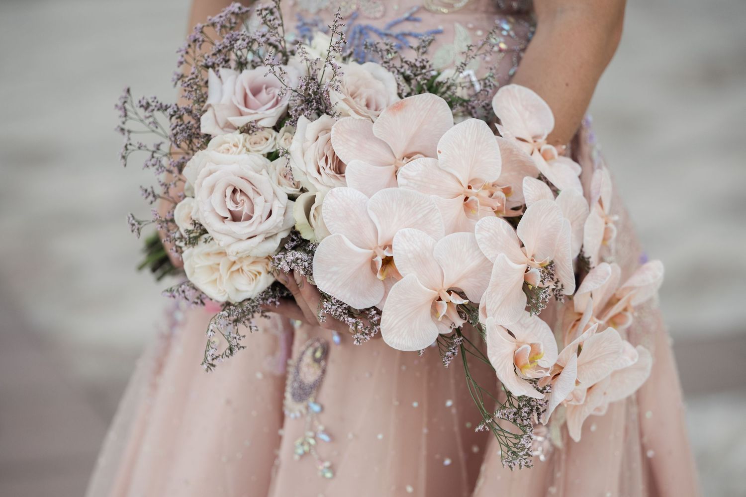 Soft pink and white bridal bouquet featuring roses and orchids with delicate silver accents.